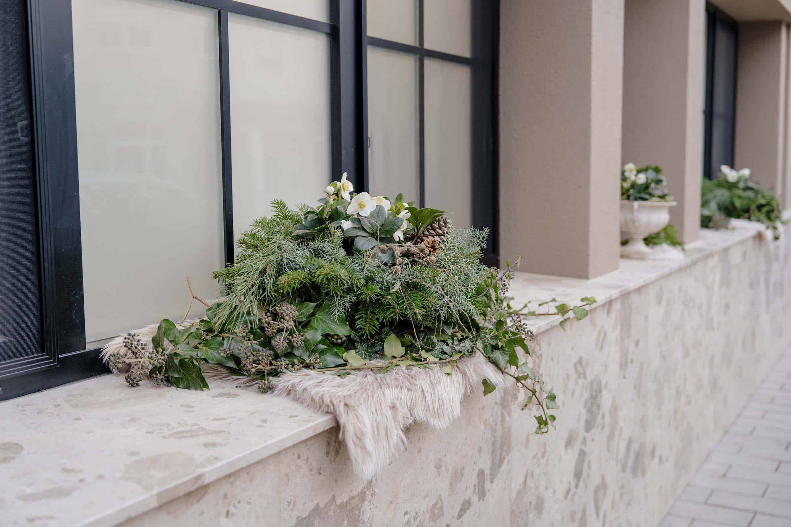 Natürliche Hochzeitsdekoration mit Nadelzweigen und weißen Blüten auf Fensterbank einer eleganten Hochzeitslocation.