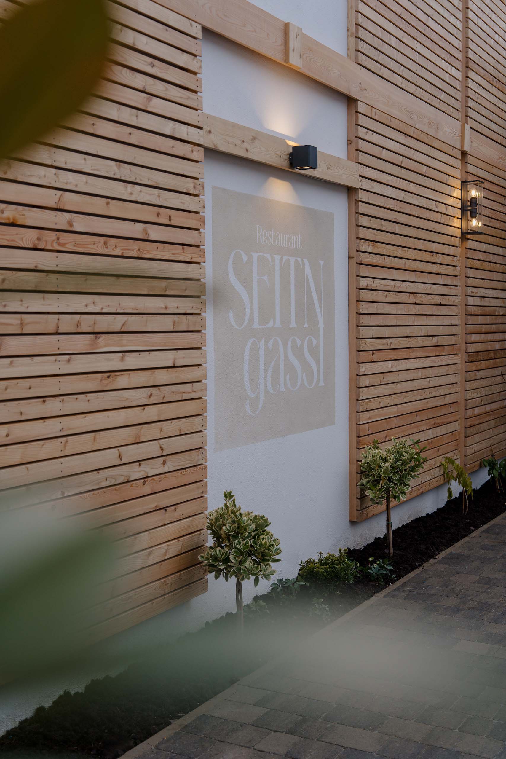 Moderne Holzwand dekoriert mit Lampen und Pflanzen, ideal für eine stilvolle Hochzeit in der Location Seitngassi.