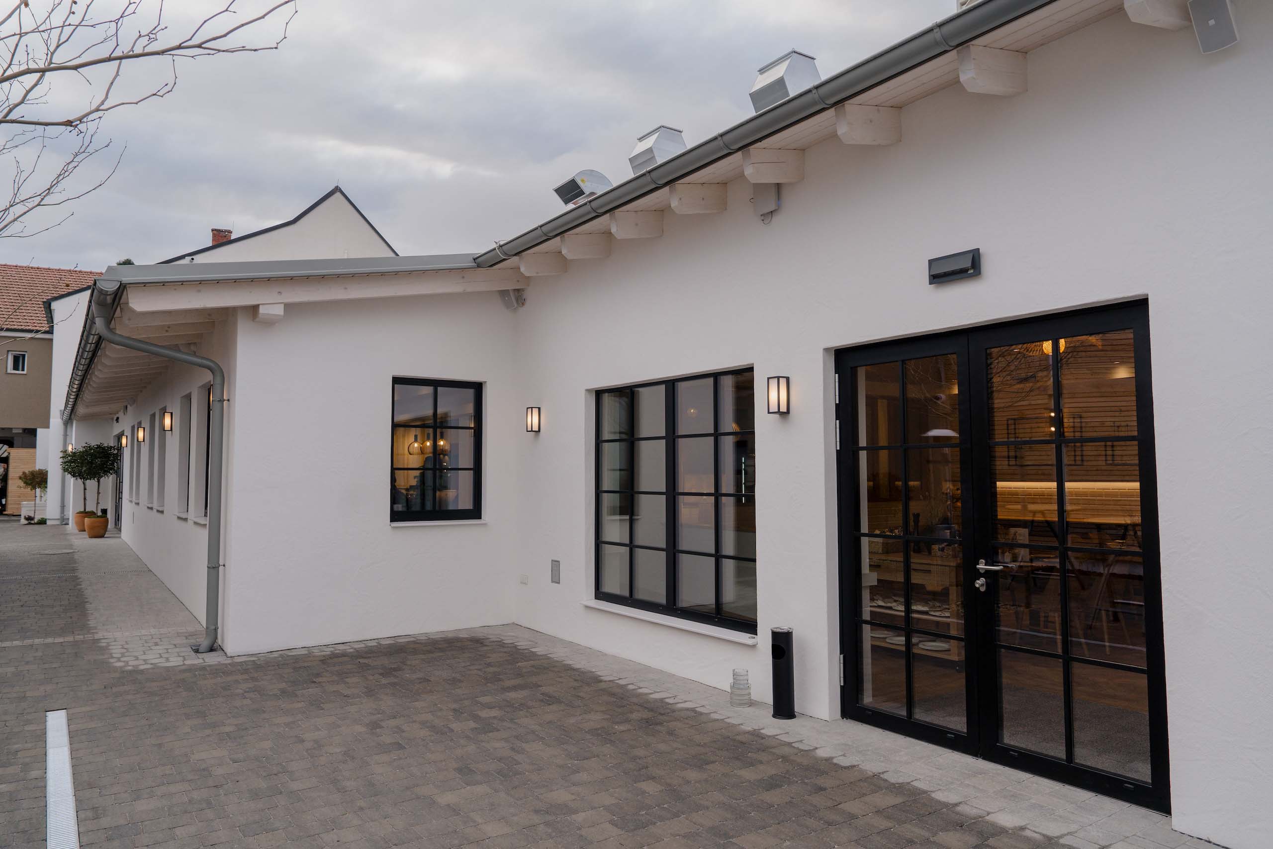 Moderner Veranstaltungsraum mit großen Fenstern, ideal für eine Hochzeitsfeier, bei bewölktem Himmel von außen gesehen.