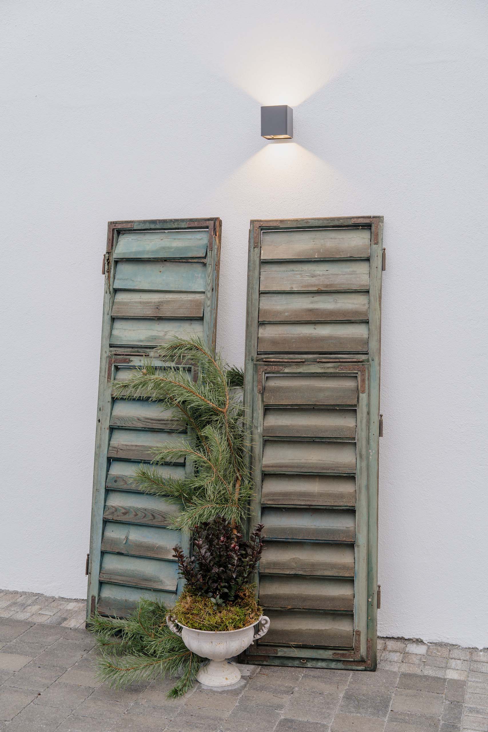 Rustikale Fensterläden, dekoriert mit grünen Zweigen, neben einer weißen Wand für eine romantische Hochzeitslocation.