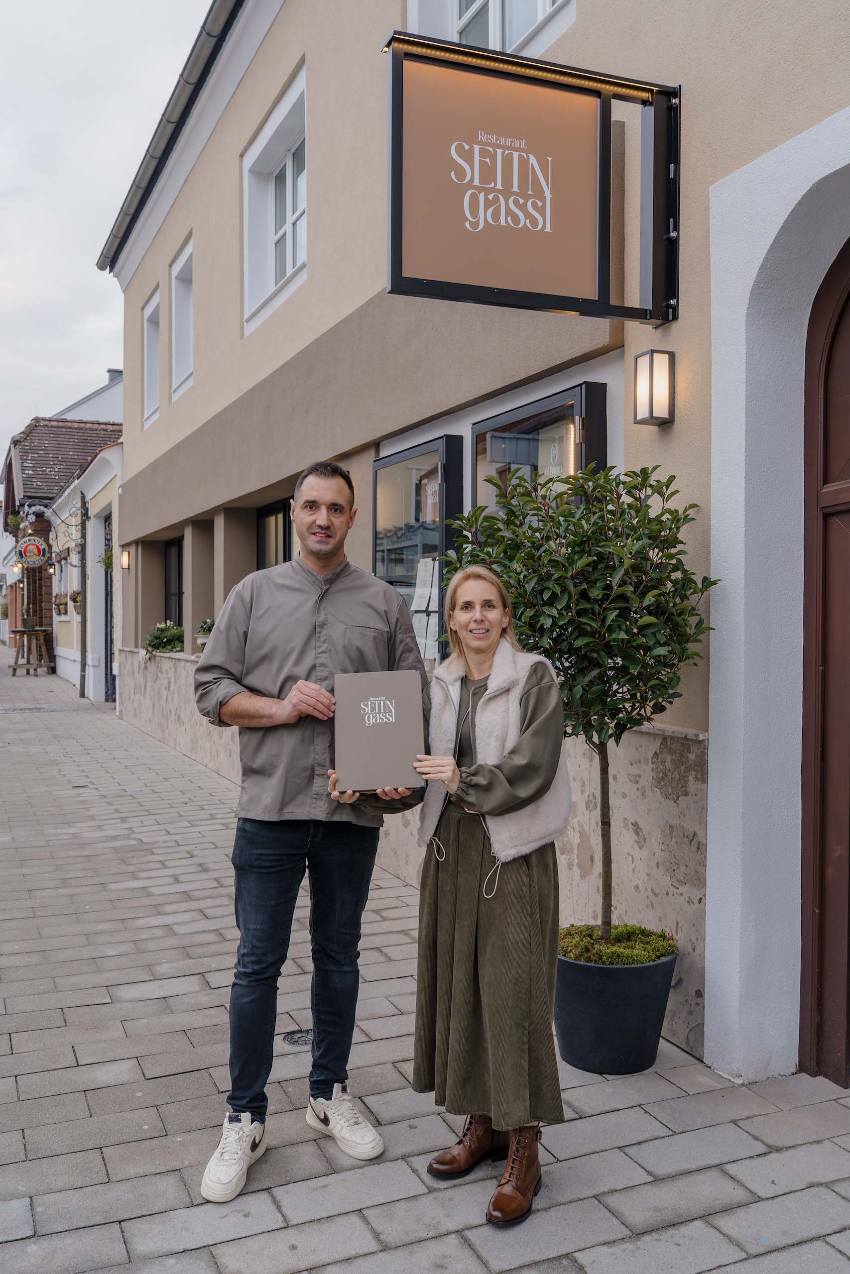 Paar vor Restaurant Seit'n Gassl—perfekte Hochzeitslocation, charmant und einladend für Ihren Hochzeitstraum.