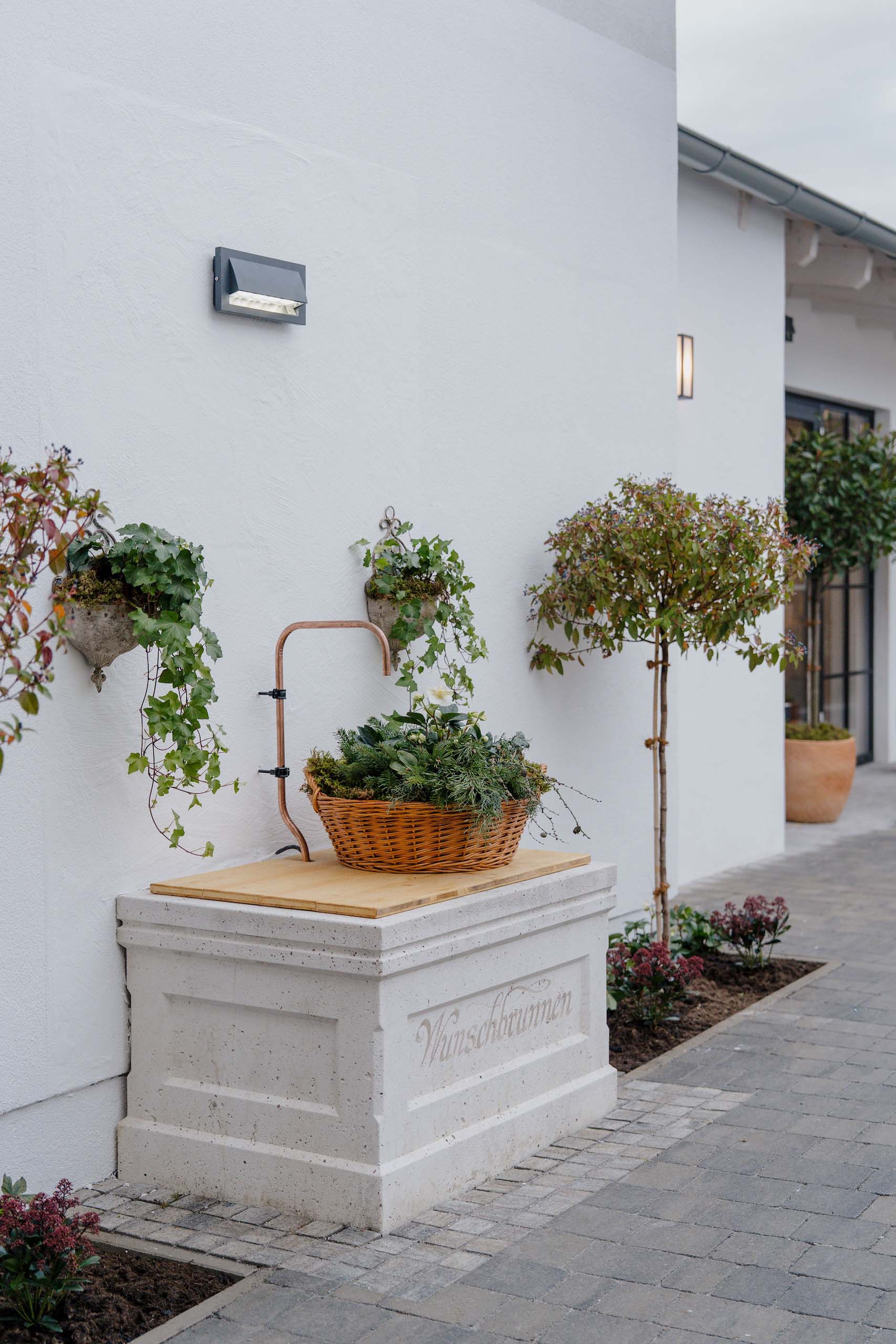 Außenansicht einer eleganten Hochzeitslocation mit bepflanztem Wunschbrunnen und einladender Dekoration.