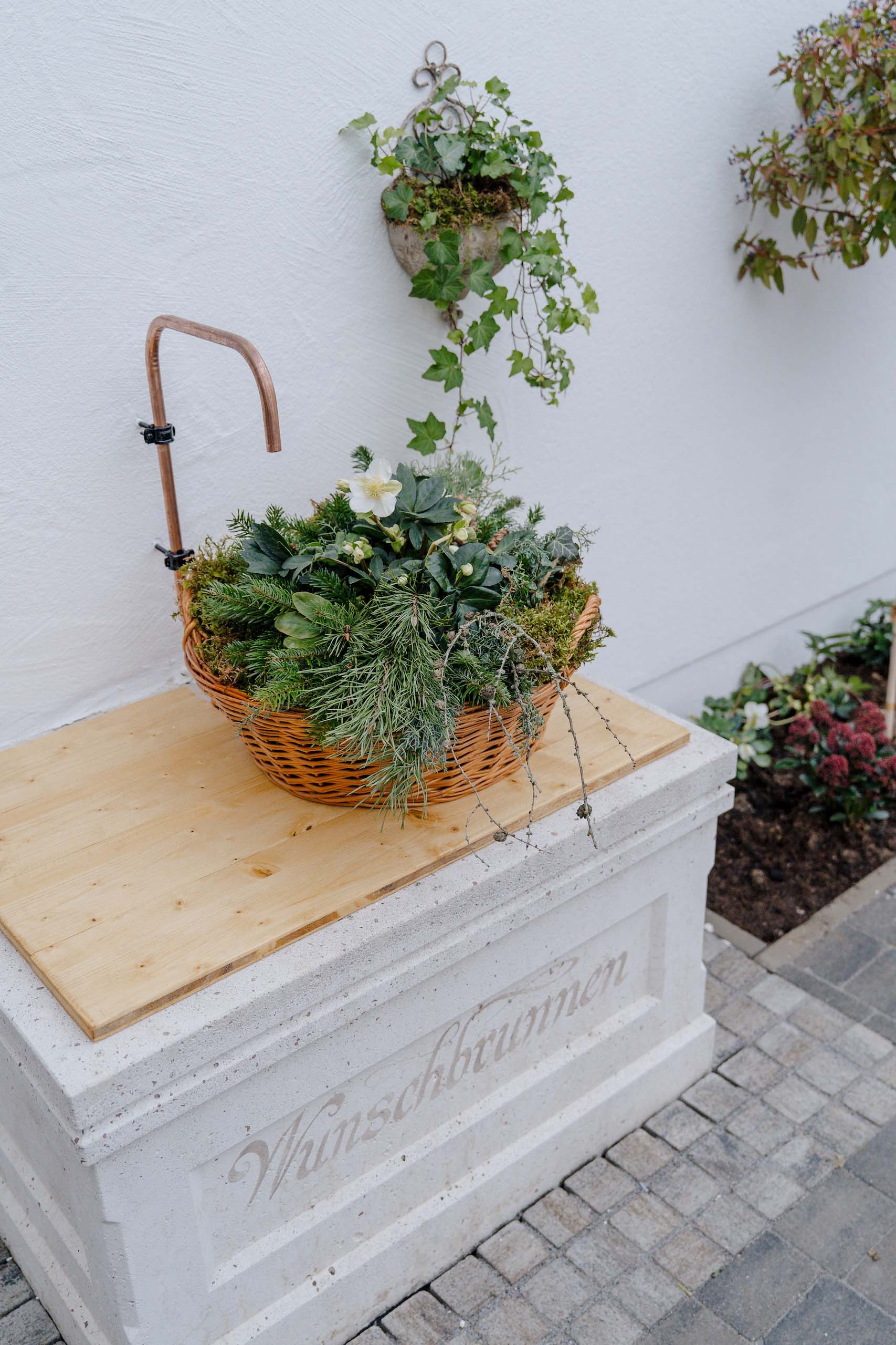 Romantischer Wunschbrunnen mit grünem Blumenkorb, ideal für eine traumhafte Hochzeitslocation im Freien.