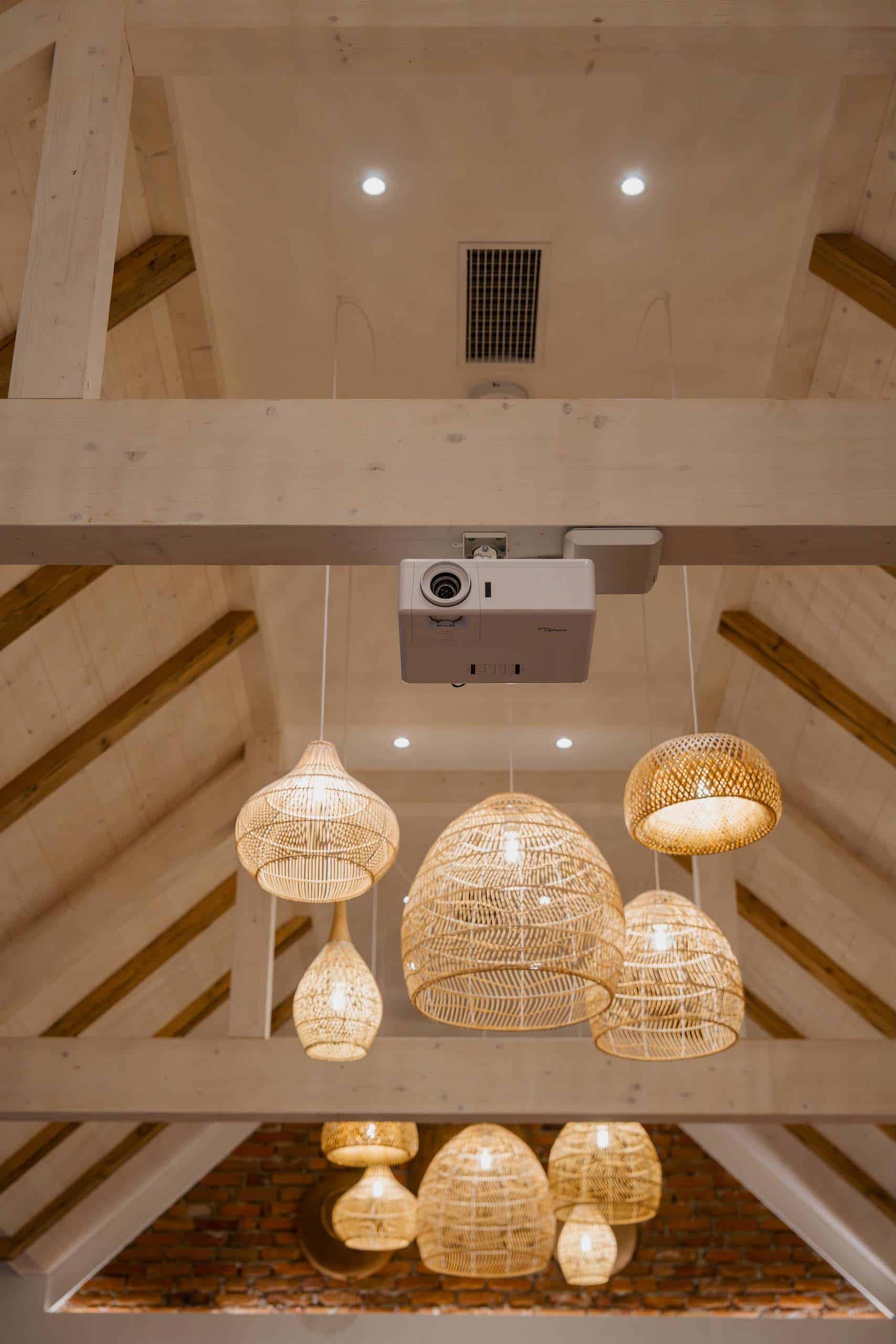 Rattan-Lampen unter Holzbalkendecke in eleganter Hochzeitslocation, ideal für eine traumhafte Feier.