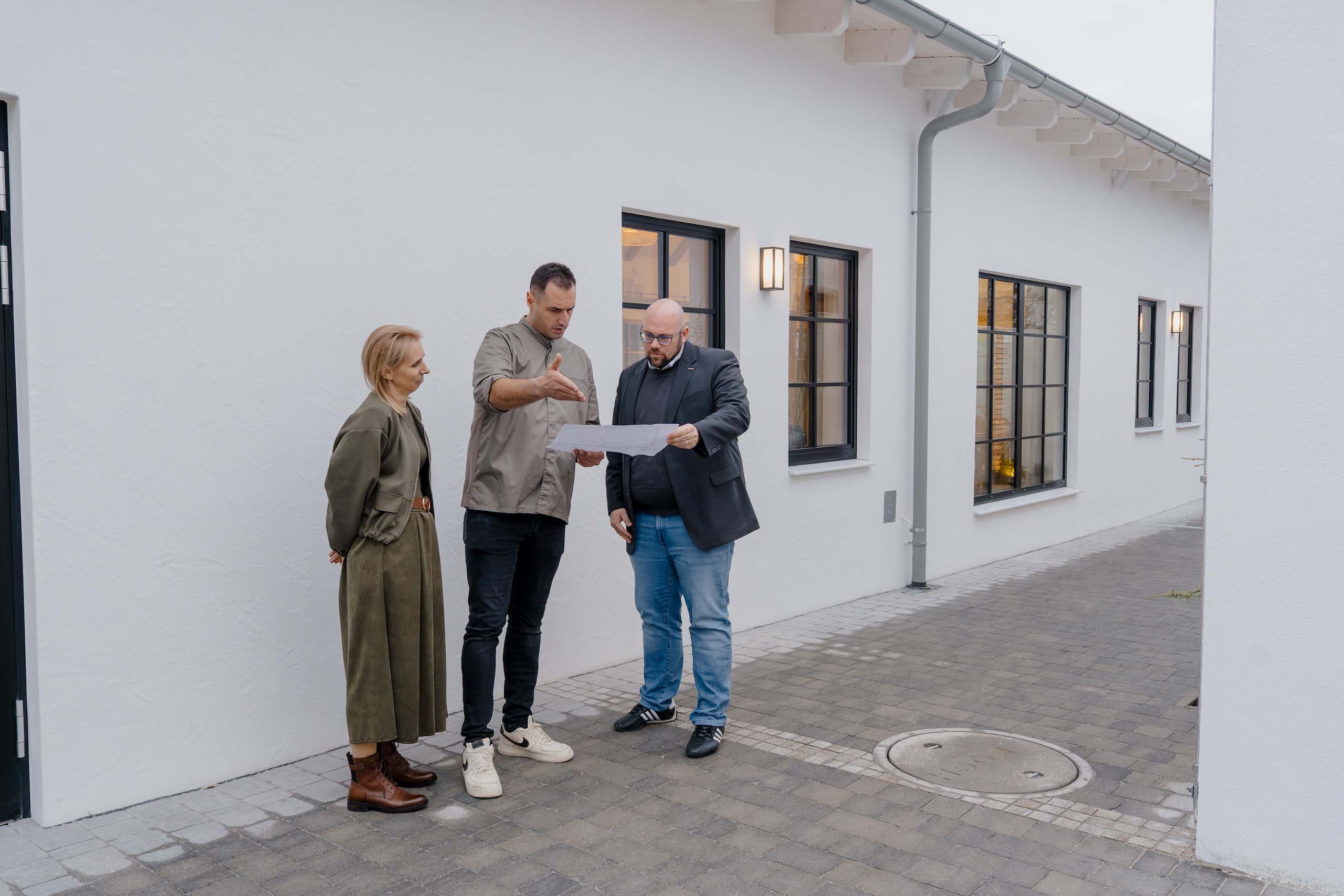 Gruppe bespricht Hochzeitsplan vor moderner weißer Hochzeitslocation, ideal für den perfekten Hochzeitstraum.