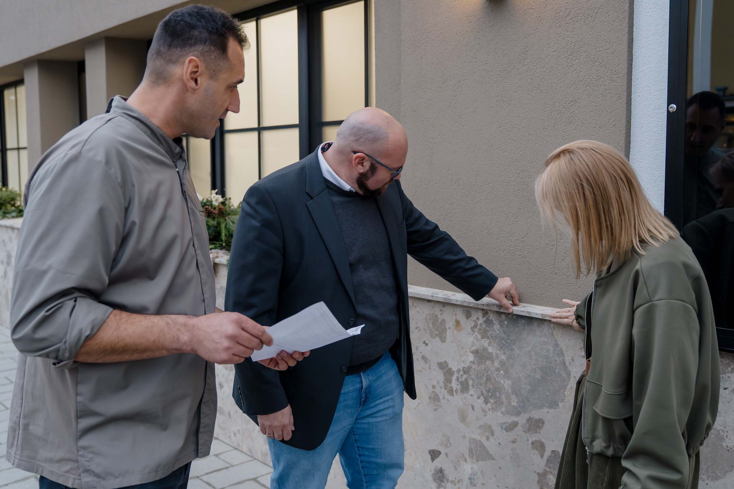 Drei Personen inspizieren die Fassade einer Hochzeitslocation im Freien, planen Details für das perfekte Hochzeitserlebnis.