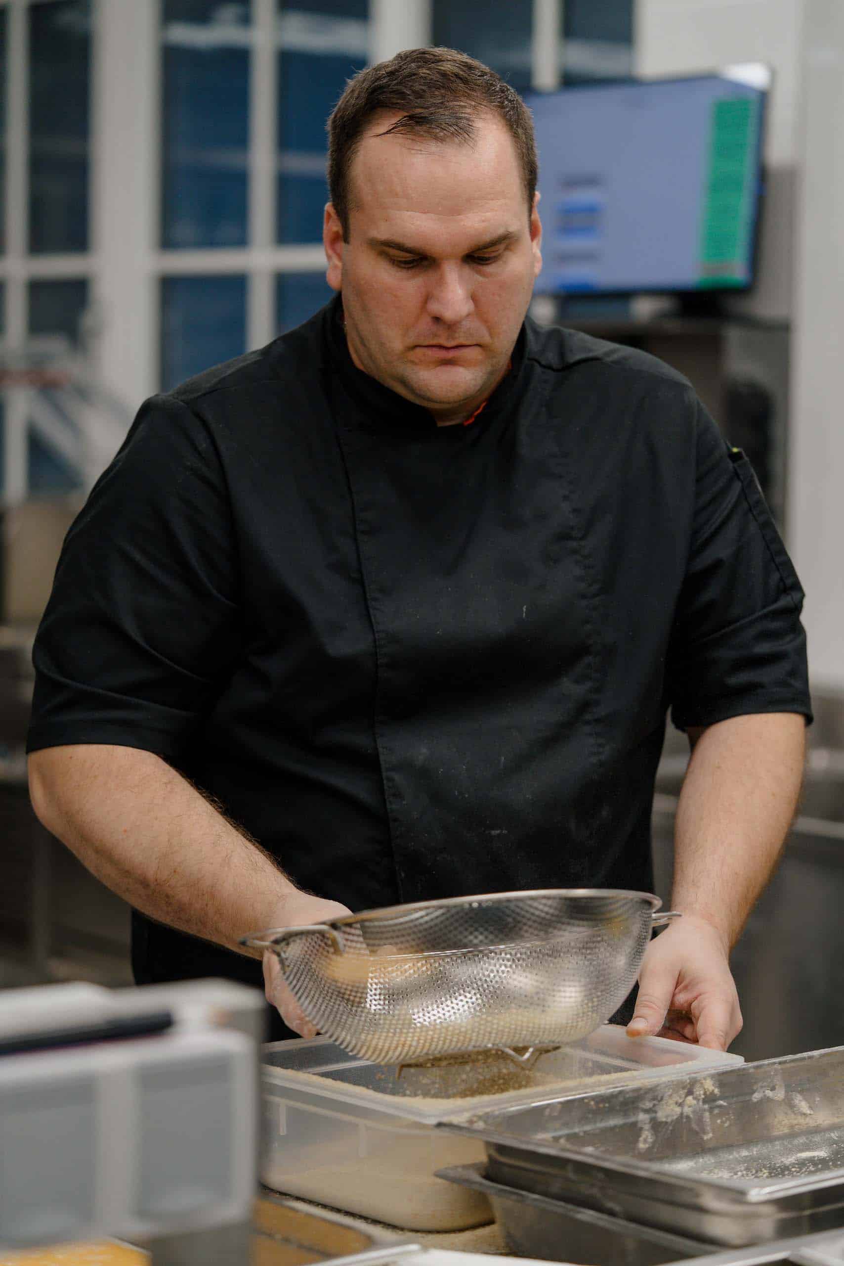Koch in Aktion: Ein Chefkoch in schwarzer Uniform bereitet Delikatessen für eine elegante Hochzeitsfeier vor.