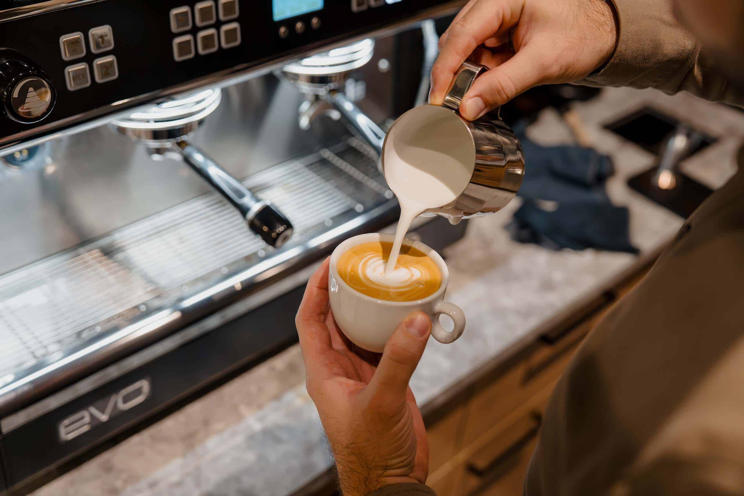 Barista zaubert kunstvollen Cappuccino für Hochzeitsgäste, perfekte Ergänzung zur Traumhochzeitslocation.
