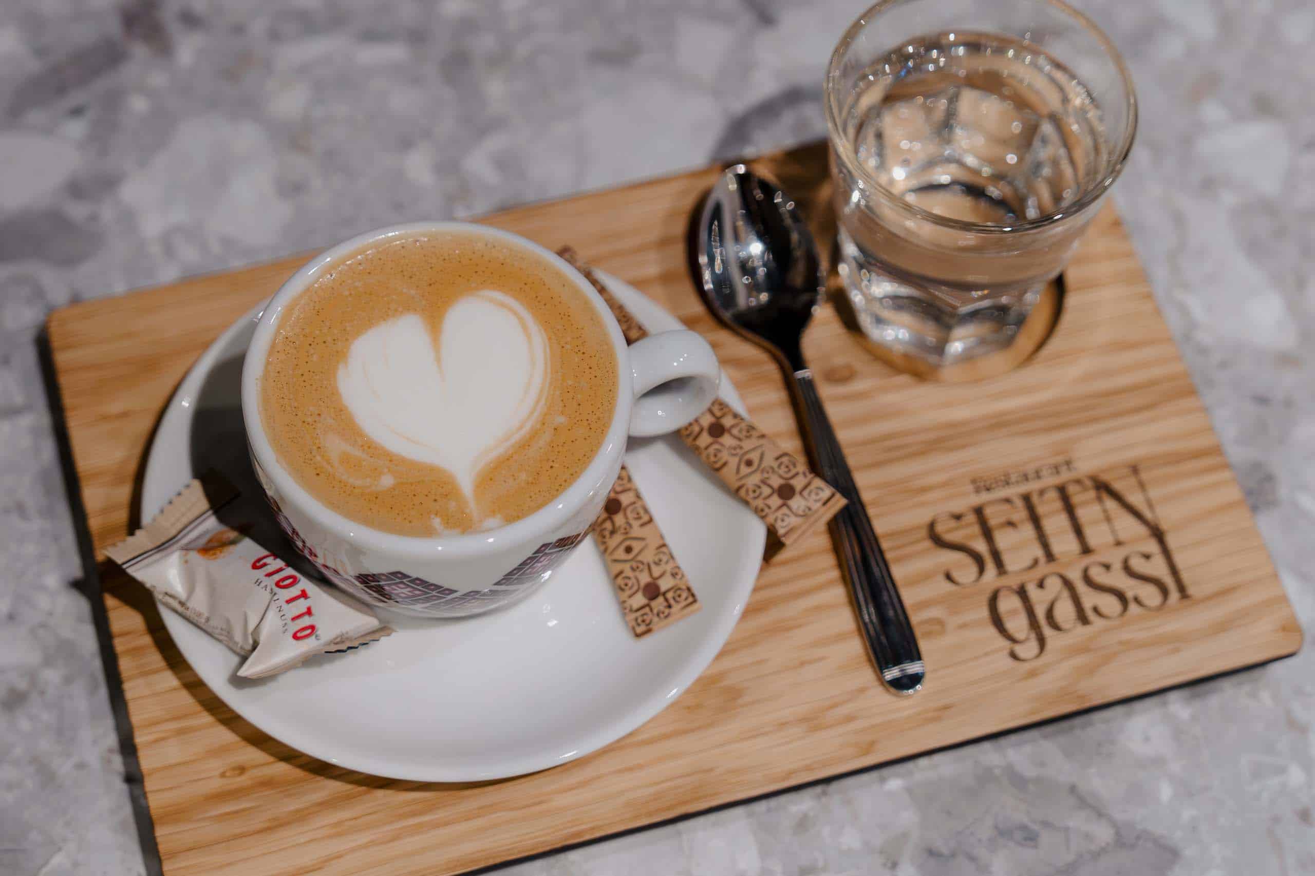 Cappuccino mit Herz-Latte-Art, serviert auf Holztablett mit Keks, ideal für Hochzeiten oder romantische Anlässe.
