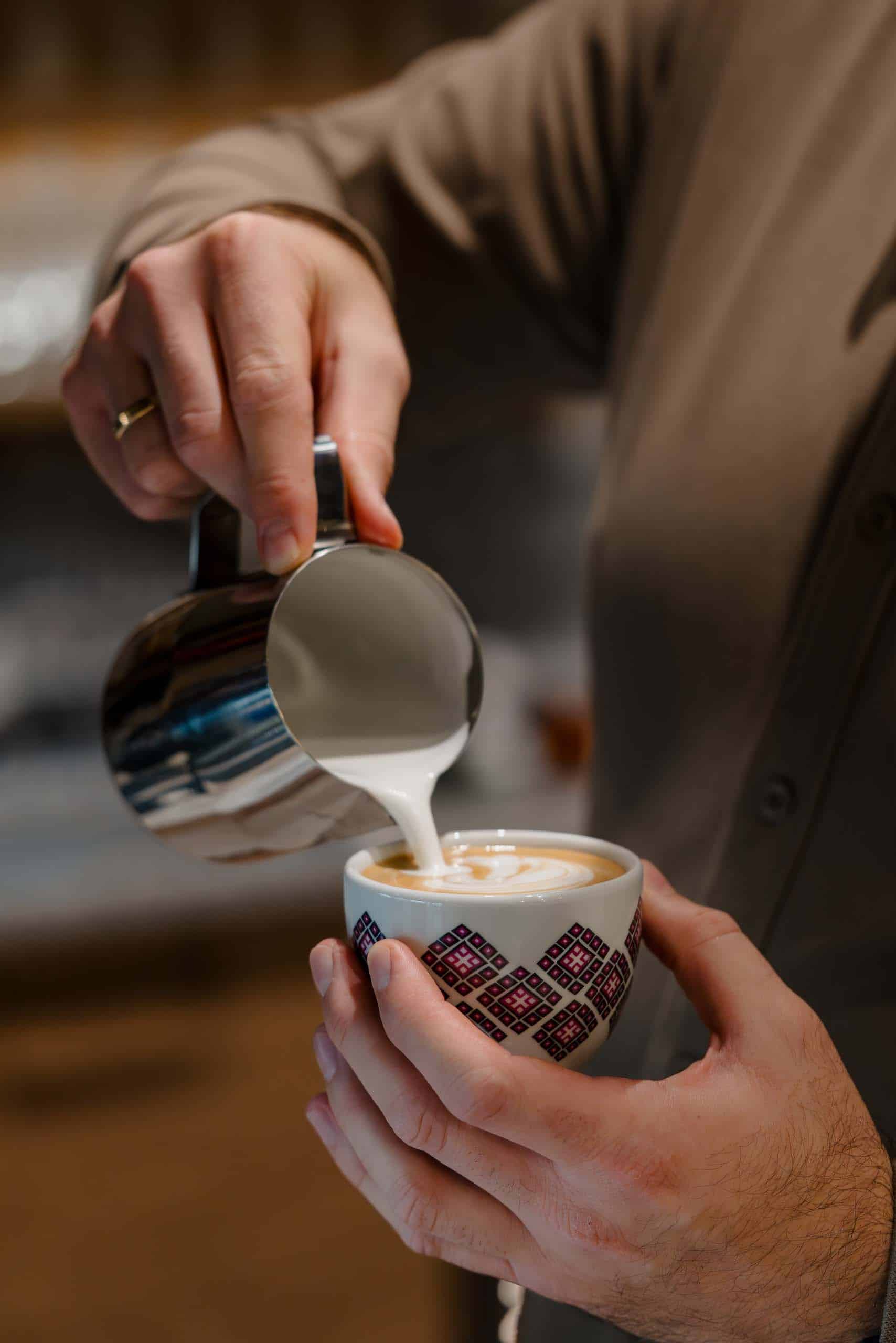 Barista gießt Milchschaum in eine kunstvoll gestaltete Hochzeitstasse für eine stilvolle Hochzeitslocation.