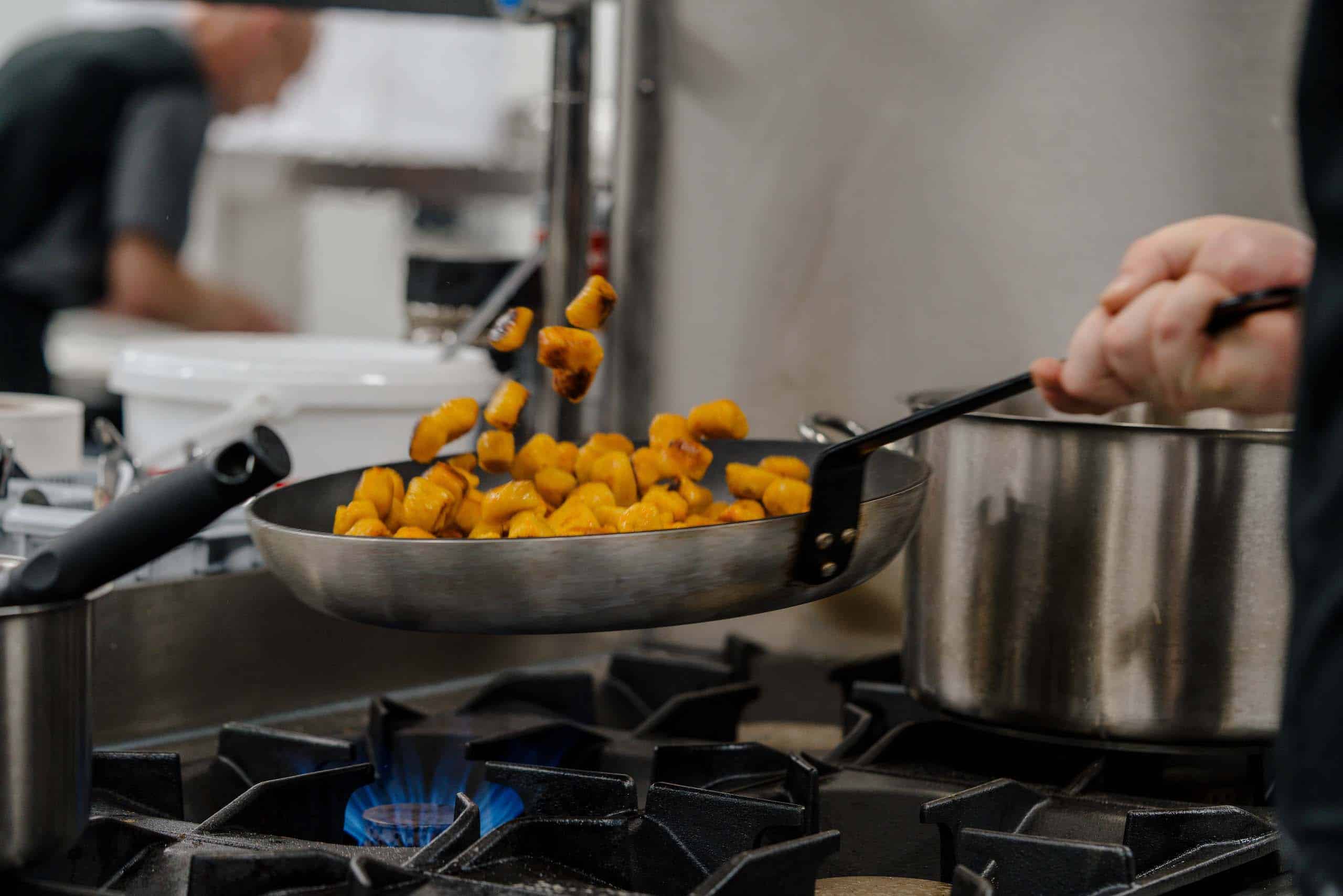 Hochzeitsküche: Koch brät leckere Speisen in Pfanne, ideal für traumhafte Hochzeitsfeiern in stilvoller Location.
