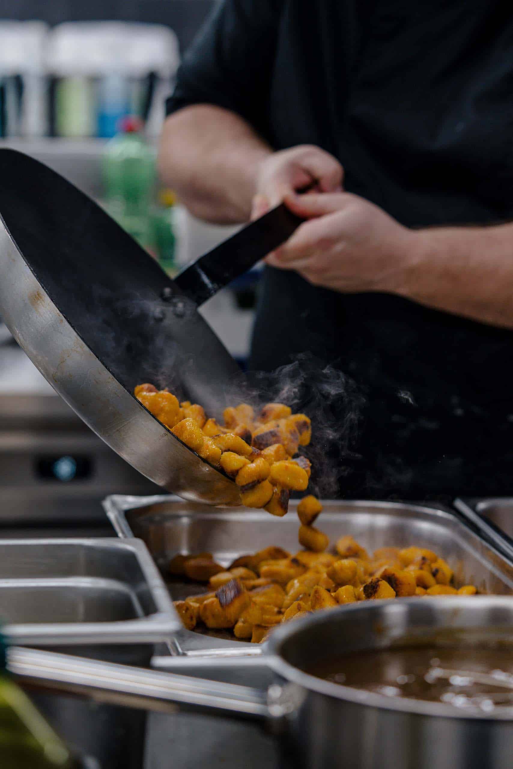 Koch bereitet dampfende Gnocchi für elegantes Hochzeitscatering in einer stilvollen Hochzeitslocation zu.