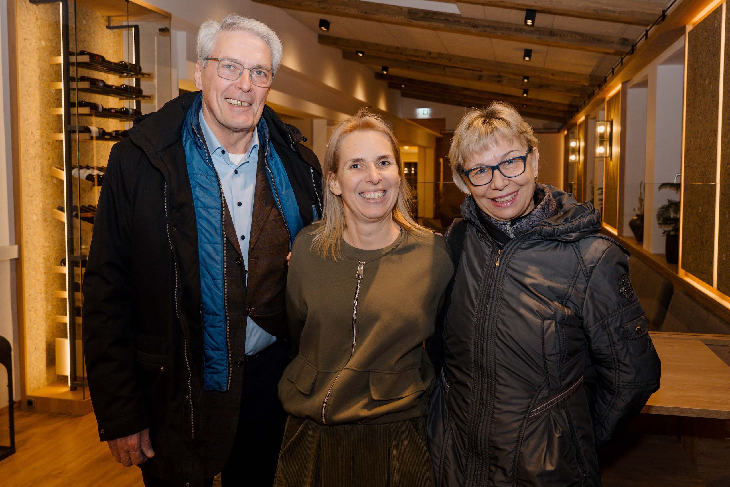 Drei lächelnde Menschen posieren in einer stilvollen Hochzeitlocation mit Holzdekor, ideal für den perfekten Hochzeitstraum.