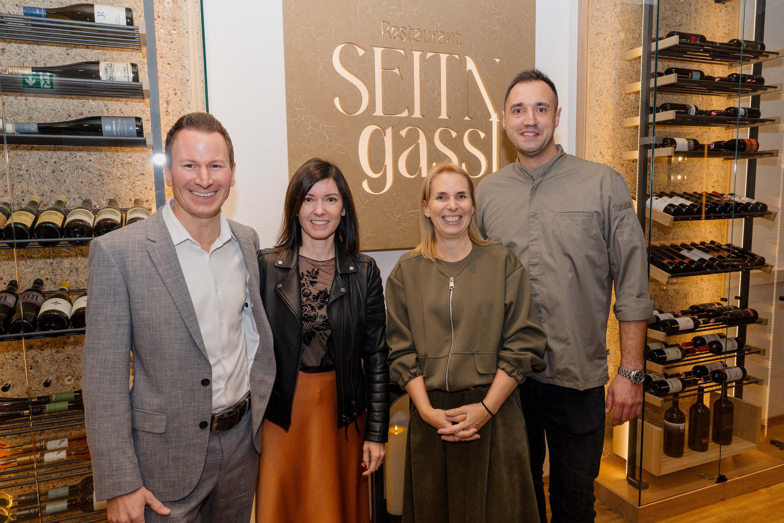 Gruppe lächelnder Menschen in eleganter Location, ideal für Hochzeiten, vor Weinregalen und Restaurant Schild.