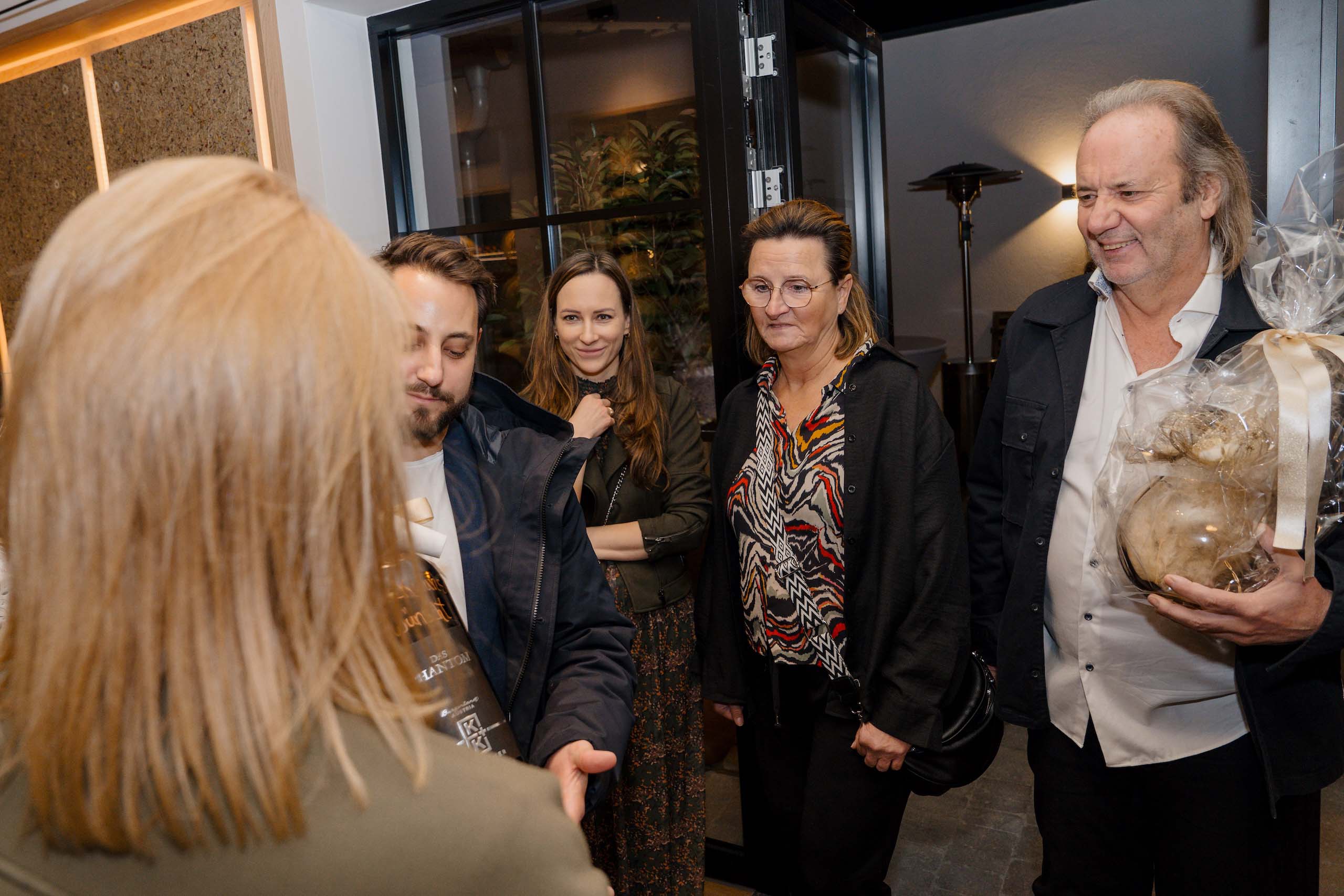 Gruppe von Hochzeitsgästen bei der Ankunft in einer stilvollen Hochzeitslocation, einer trägt ein Geschenk.