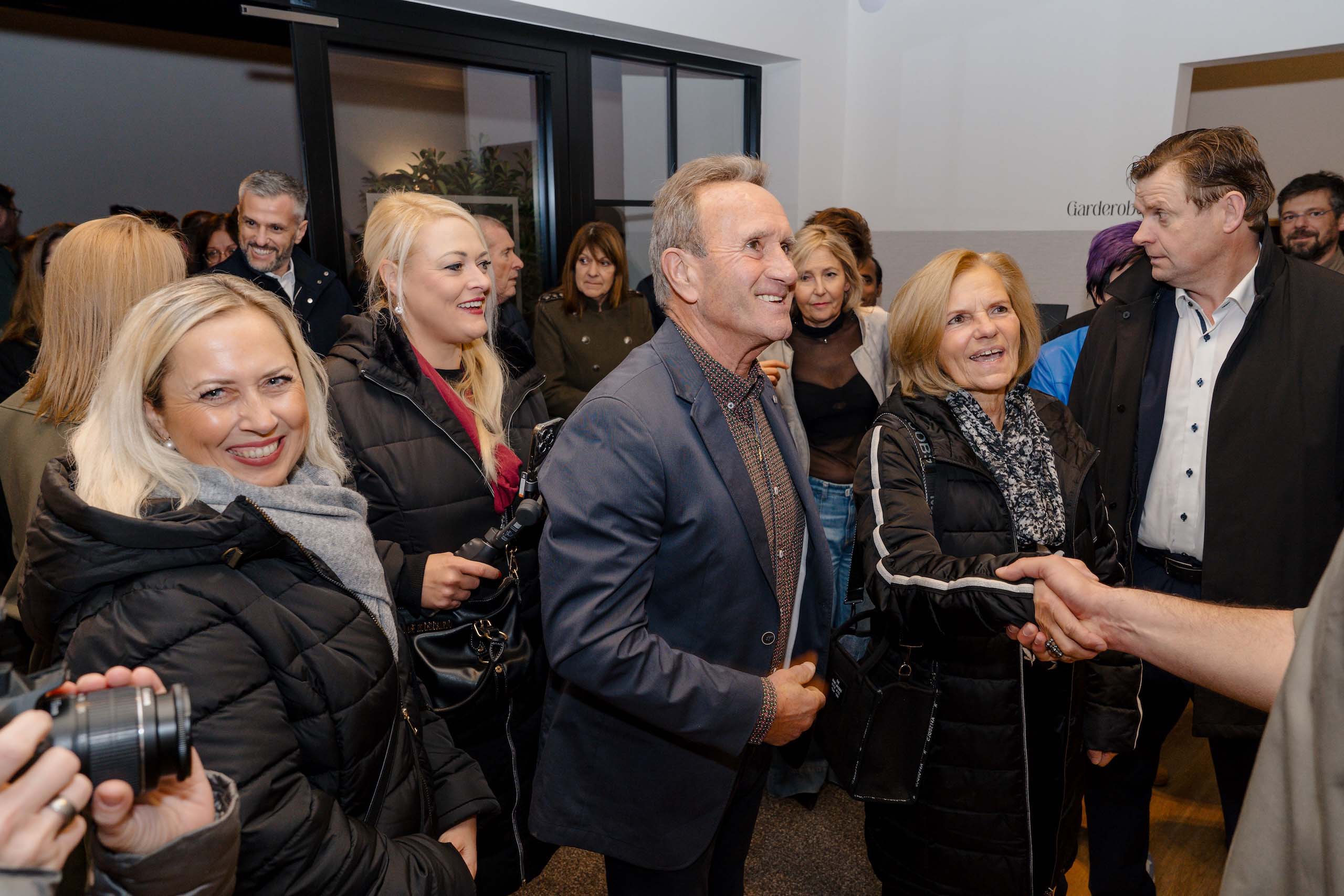 Gruppe von Gästen begrüßt sich herzlich bei einer stilvollen Hochzeitslocation-Eröffnung. Perfekte Atmosphäre für den Hochzeitstraum.