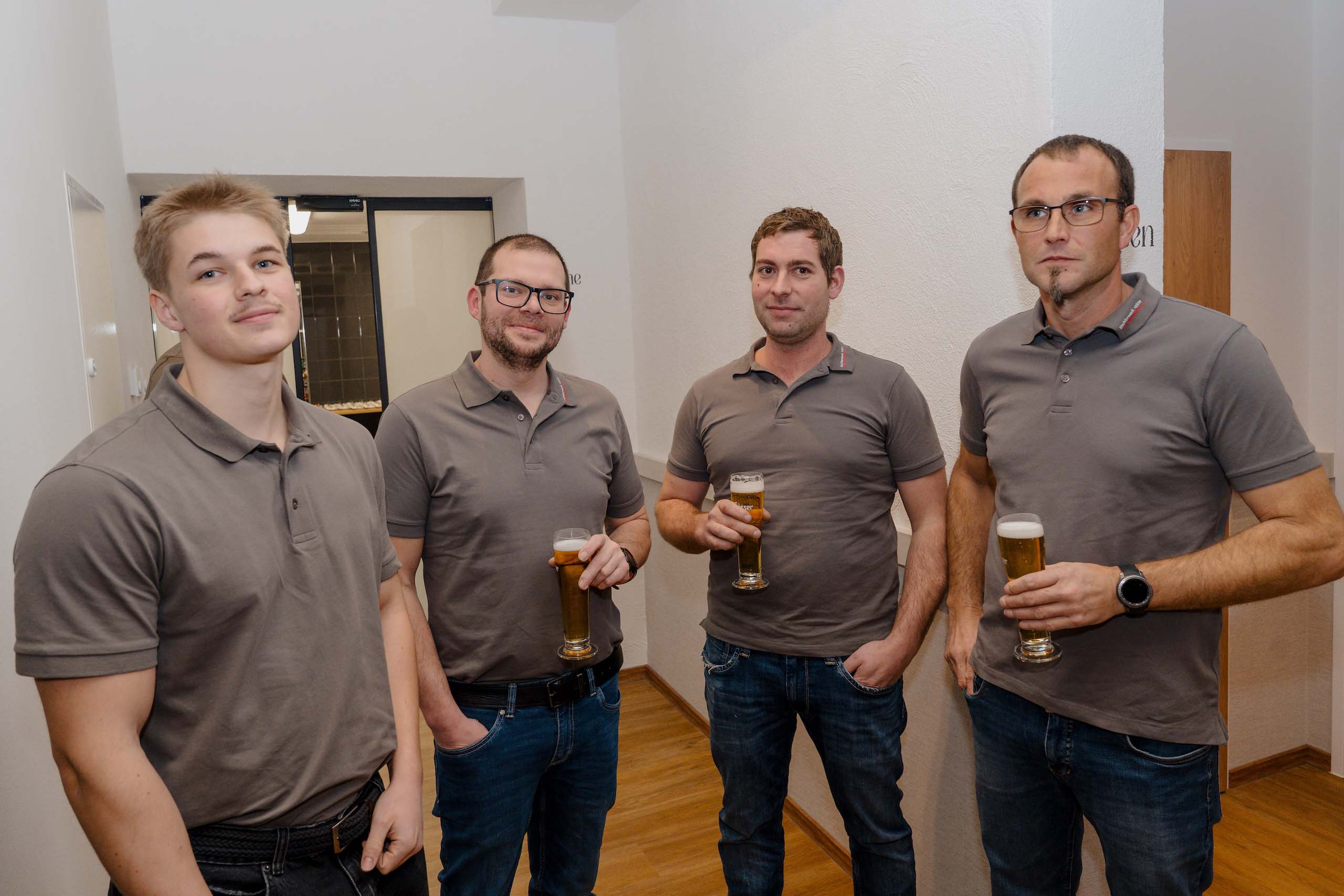 Vier Männer in grauen Poloshirts halten Biergläser bei einer Feier in der Hochzeitstraum-Location.