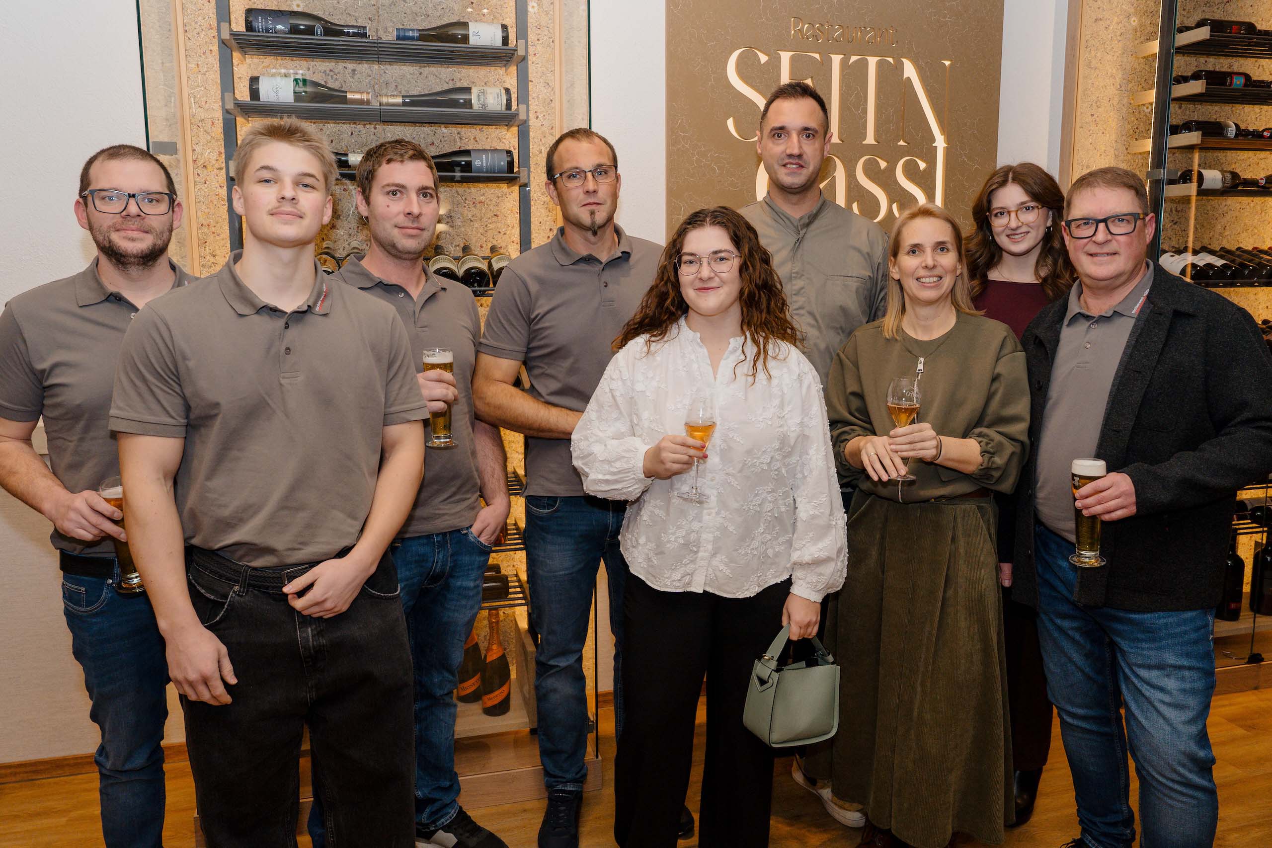 Gruppe von Menschen in eleganter Kleidung bei einer Feier in einer stilvollen Hochzeitslocation, alle halten Gläser.
