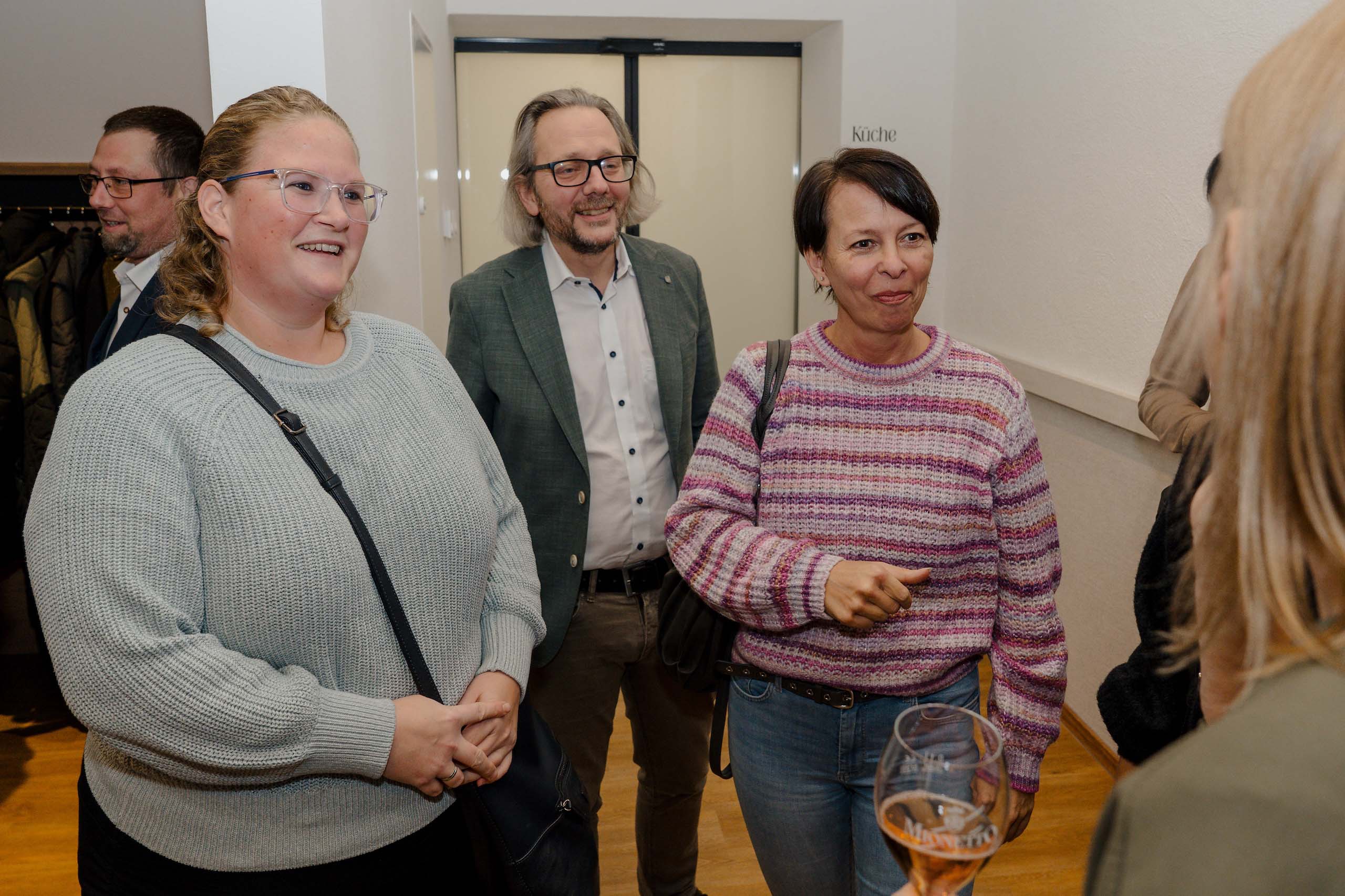 Gruppe von drei Personen in Gespräch bei Hochzeitslocation-Besichtigung, entspannte Atmosphäre, Networking über Hochzeitsträume.