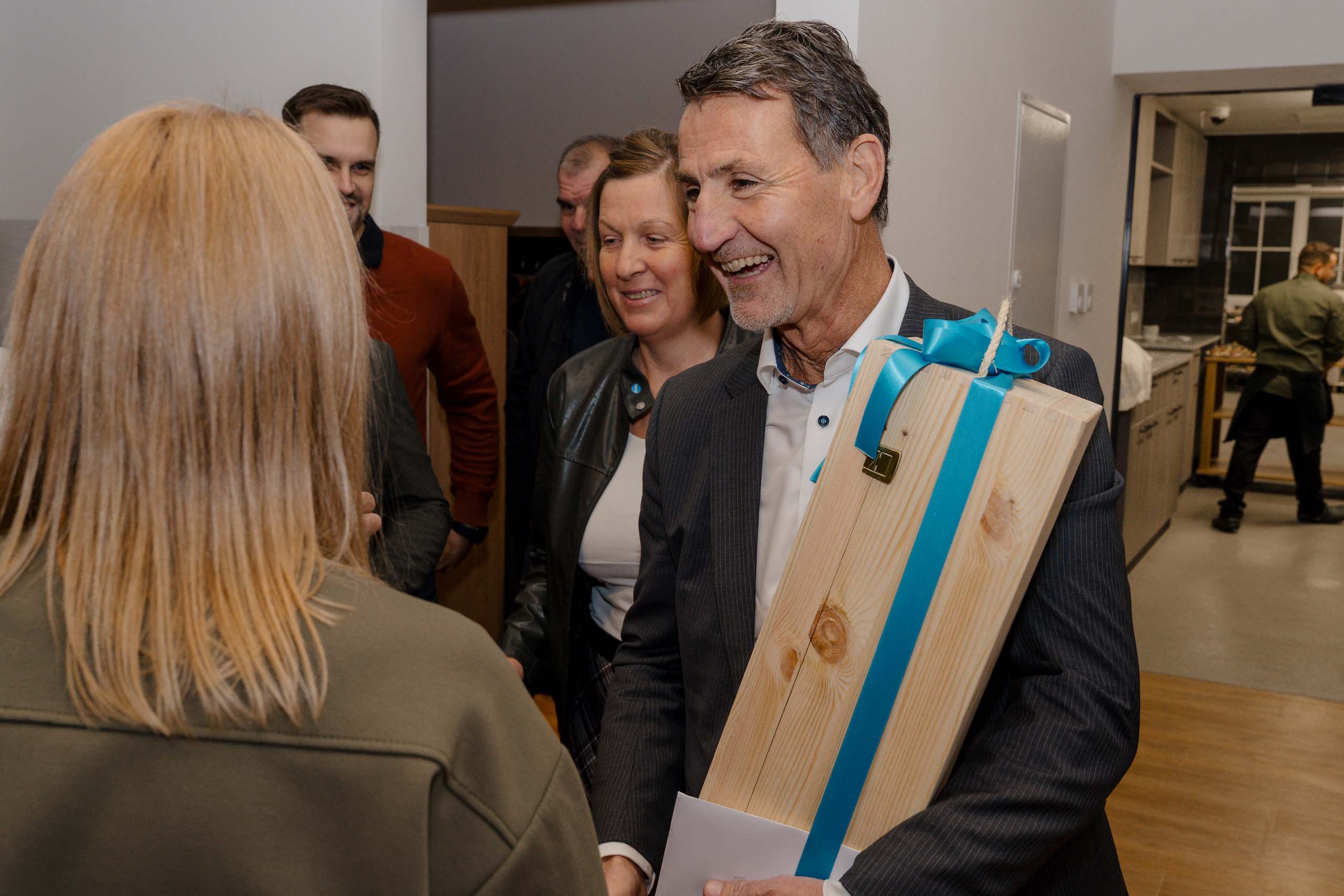 Festlich gekleideter Mann überreicht Geschenk bei Hochzeitsfeier, hell erleuchtete Atmosphäre, warme Begrüßung, Hochzeitstraum.