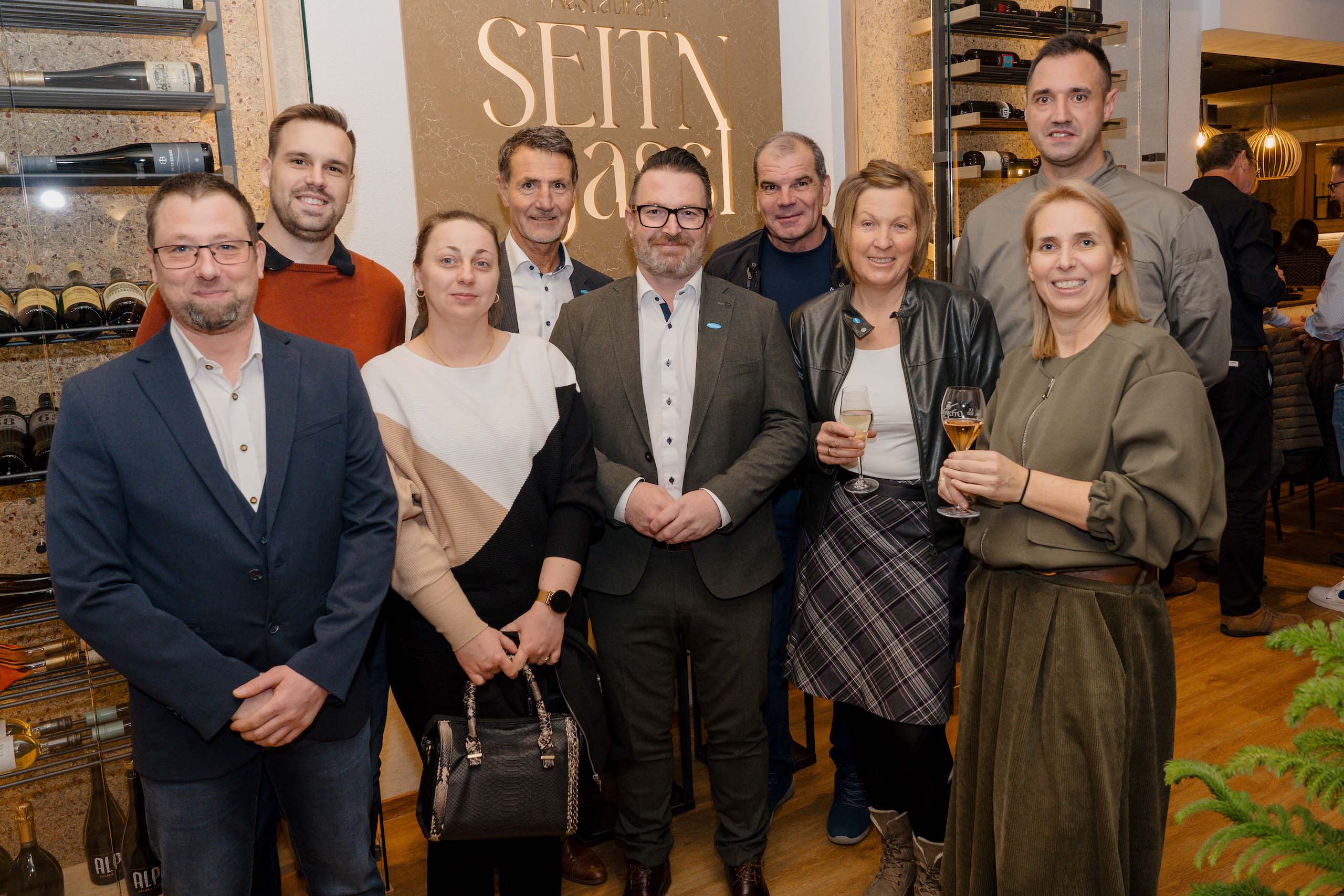 Eine Gruppe feiert fröhlich in eleganter Hochzeitslocation mit stilvoller Dekoration und Weinregalen.