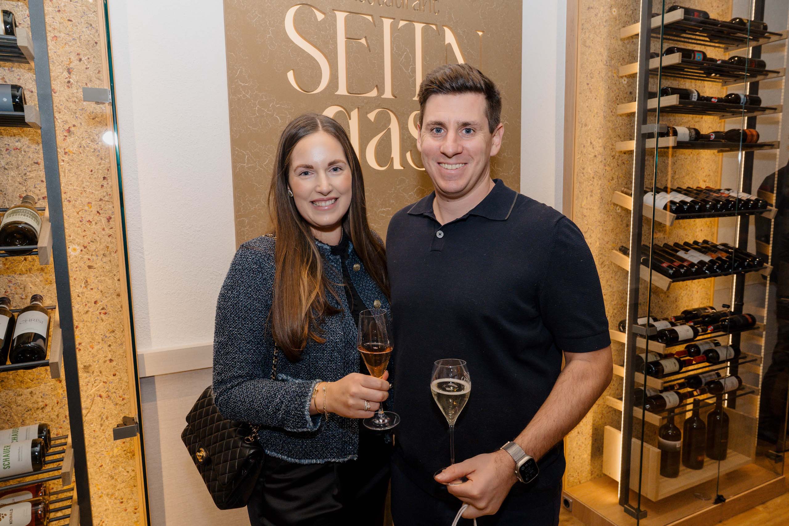 Paar im eleganten Ambiente mit Weingläsern, ideal für Hochzeitsfeier in gehobener Location, umgeben von Weinregalen.