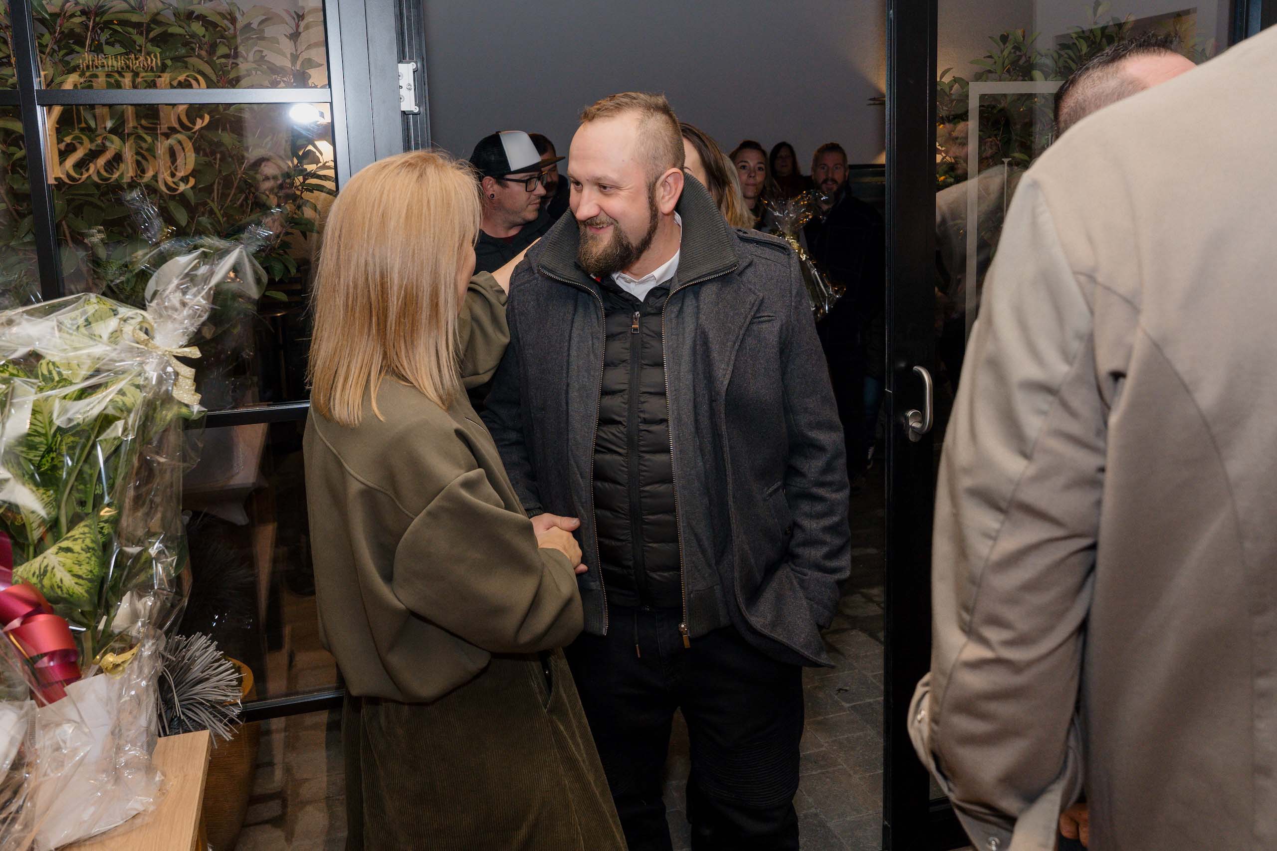 Gäste bei einer Hochzeit begrüßen sich herzlich in einer stilvollen Hochzeitslocation, umgeben von Blumenarrangements.