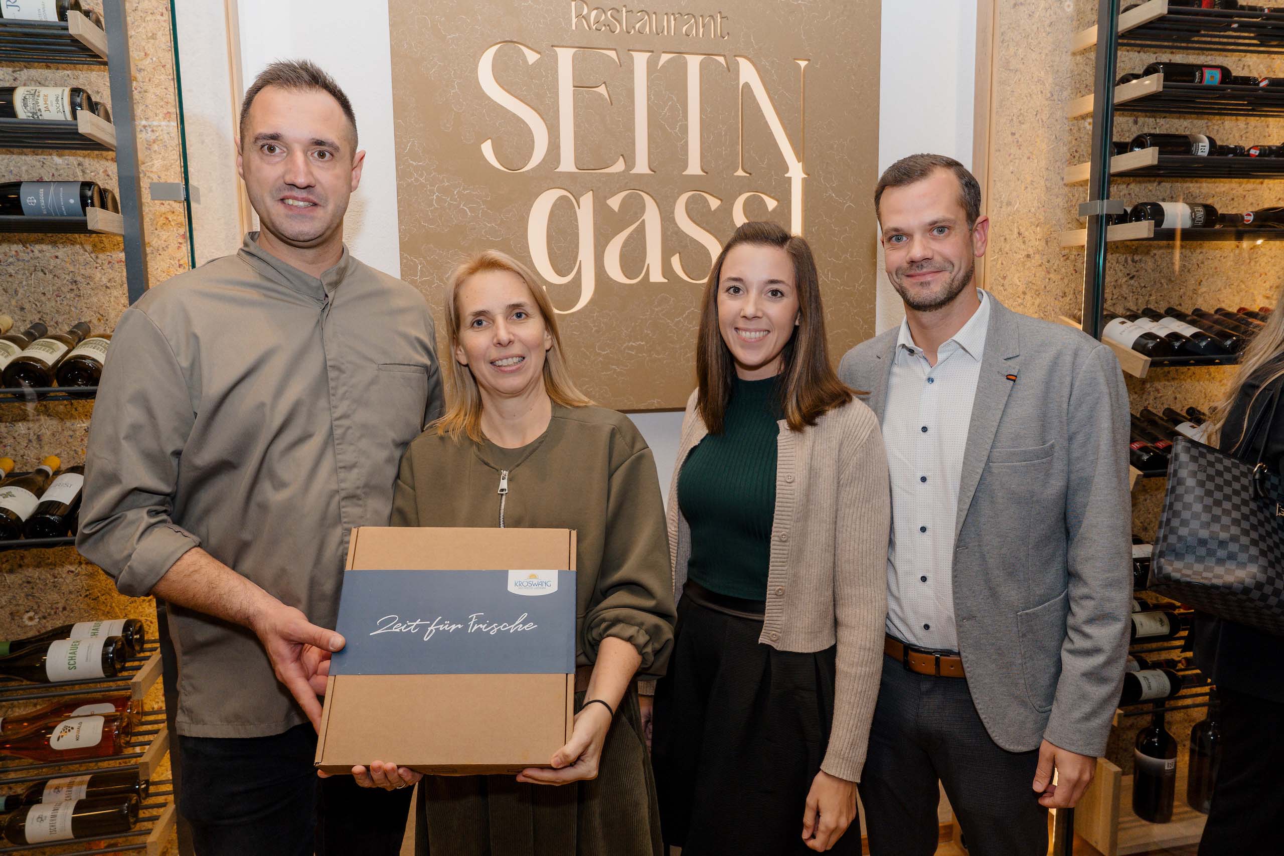 Gruppe im Restaurant, hält Geschenkbox mit Aufschrift „Zeit für Freude“. Perfekte Hochzeitslocation-Option bei Seitn gassl.