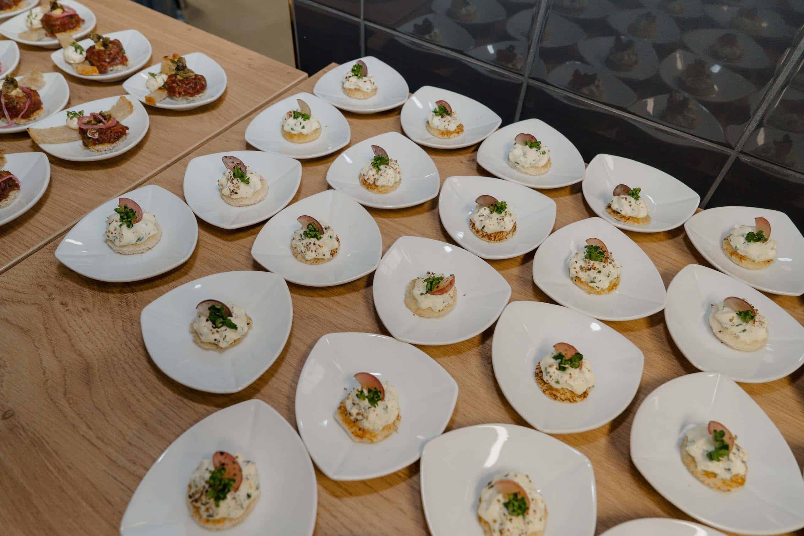 Elegante, weiße Teller mit feinen Vorspeisen für eine stilvolle Hochzeitsfeier, arrangiert auf einem Holztisch.