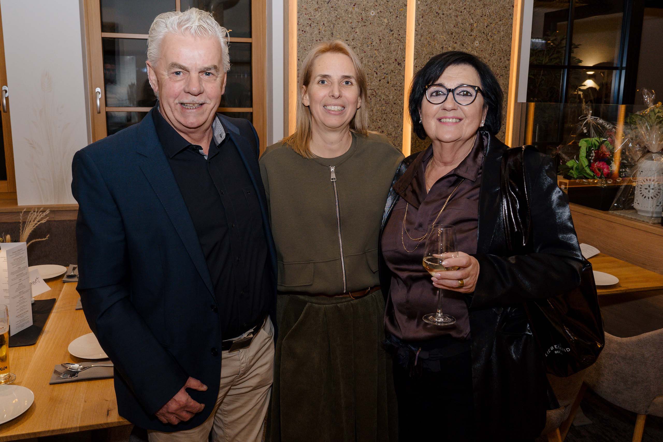 Drei lächelnde Gäste bei einer stilvollen Hochzeitsfeier, im eleganten Veranstaltungsraum einer Hochzeitslocation.