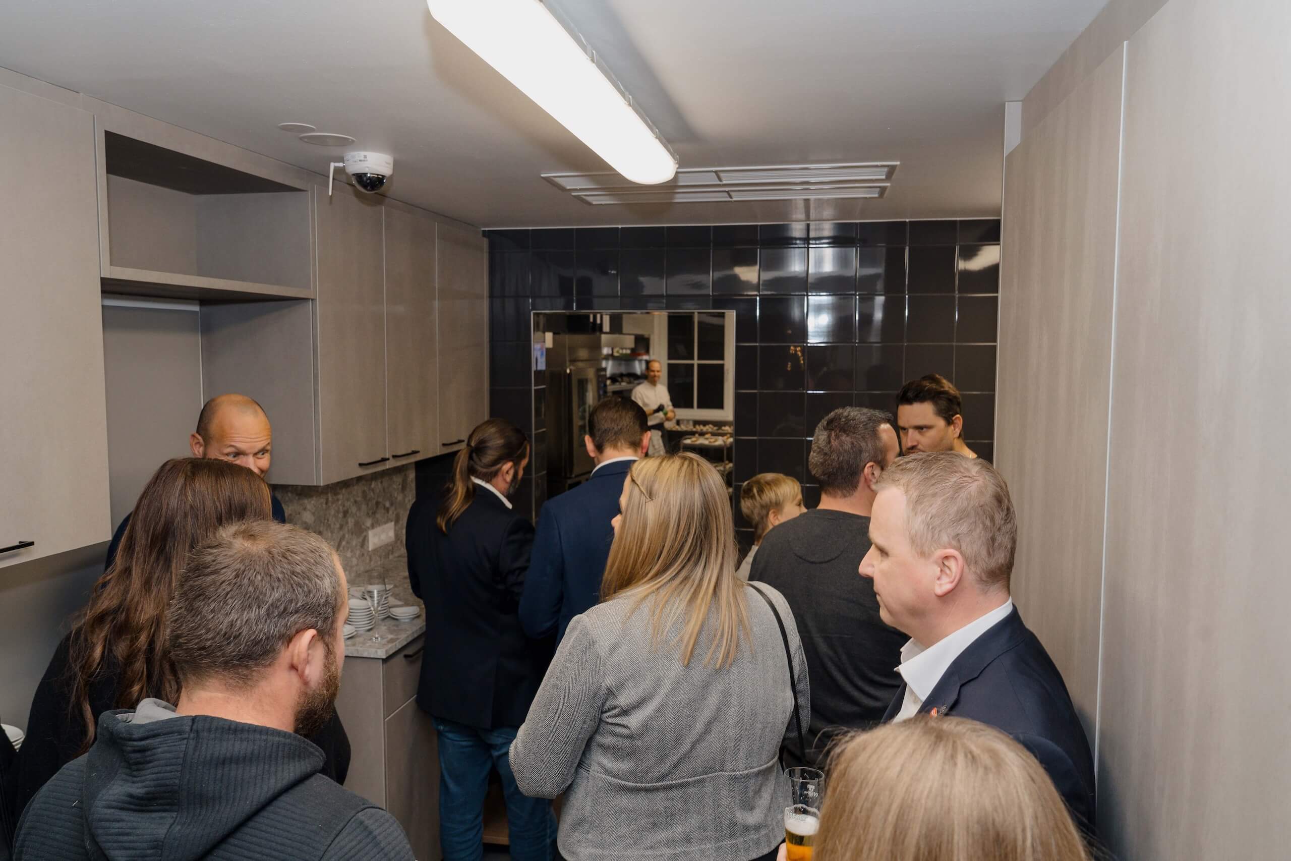 Gruppe von Gästen versammelt sich in moderner Küche, während einer Hochzeit in stilvoller Hochzeitslocation.