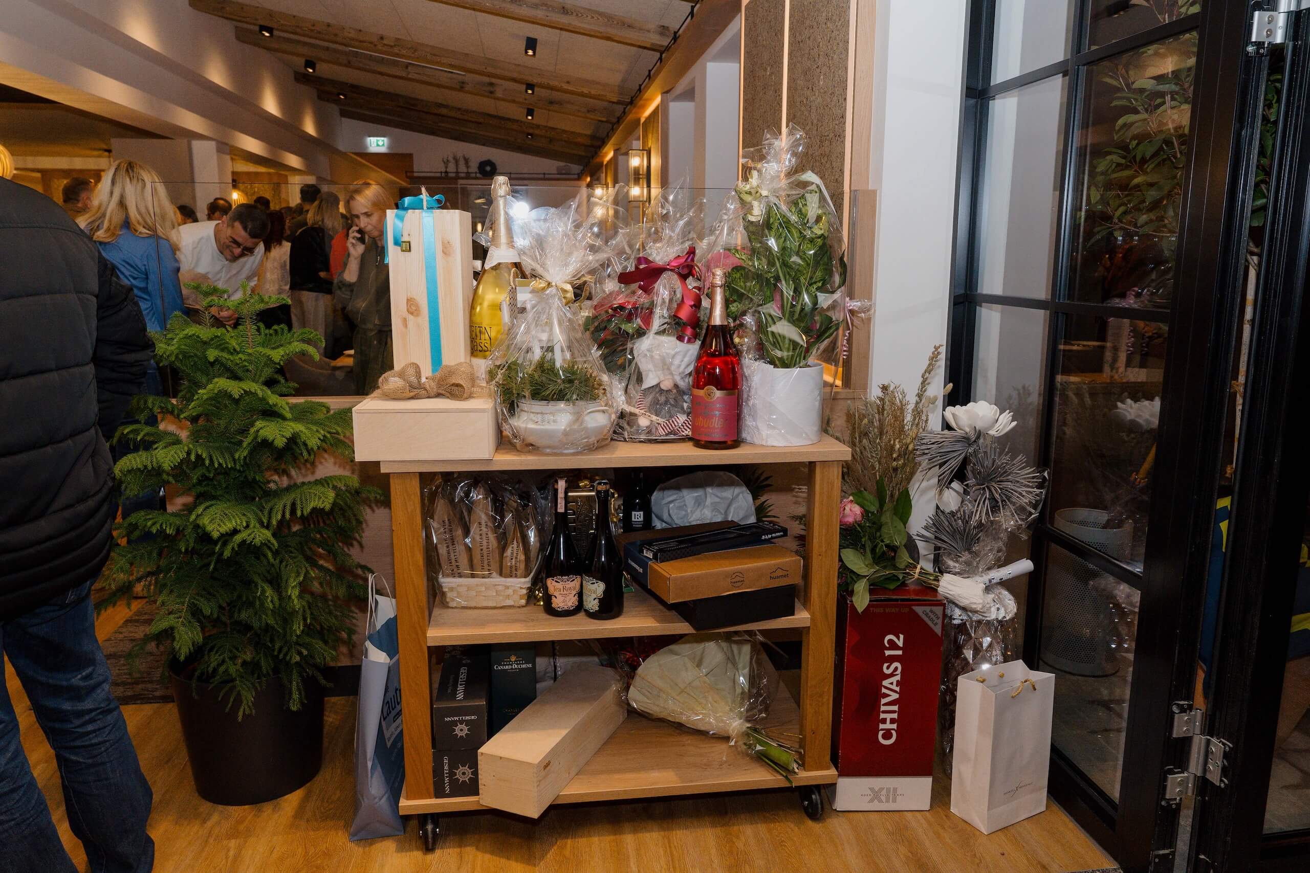 Hochzeitslocation mit dekorativen Blumen, Geschenken und Sektflaschen, umgeben von Gästen in festlicher Atmosphäre.