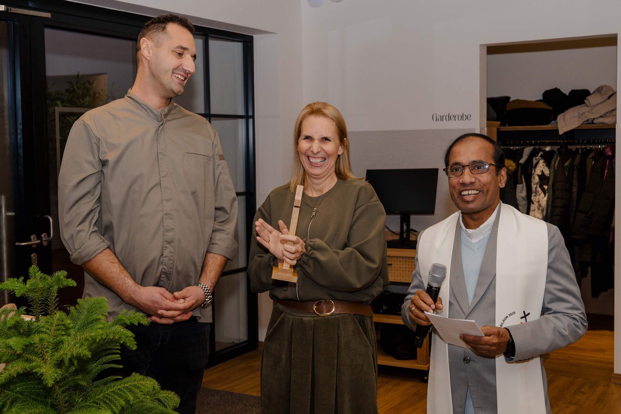 Drei lächelnde Personen bei der Eröffnung einer Hochzeitslocation, darunter ein Mann mit Mikrofon.