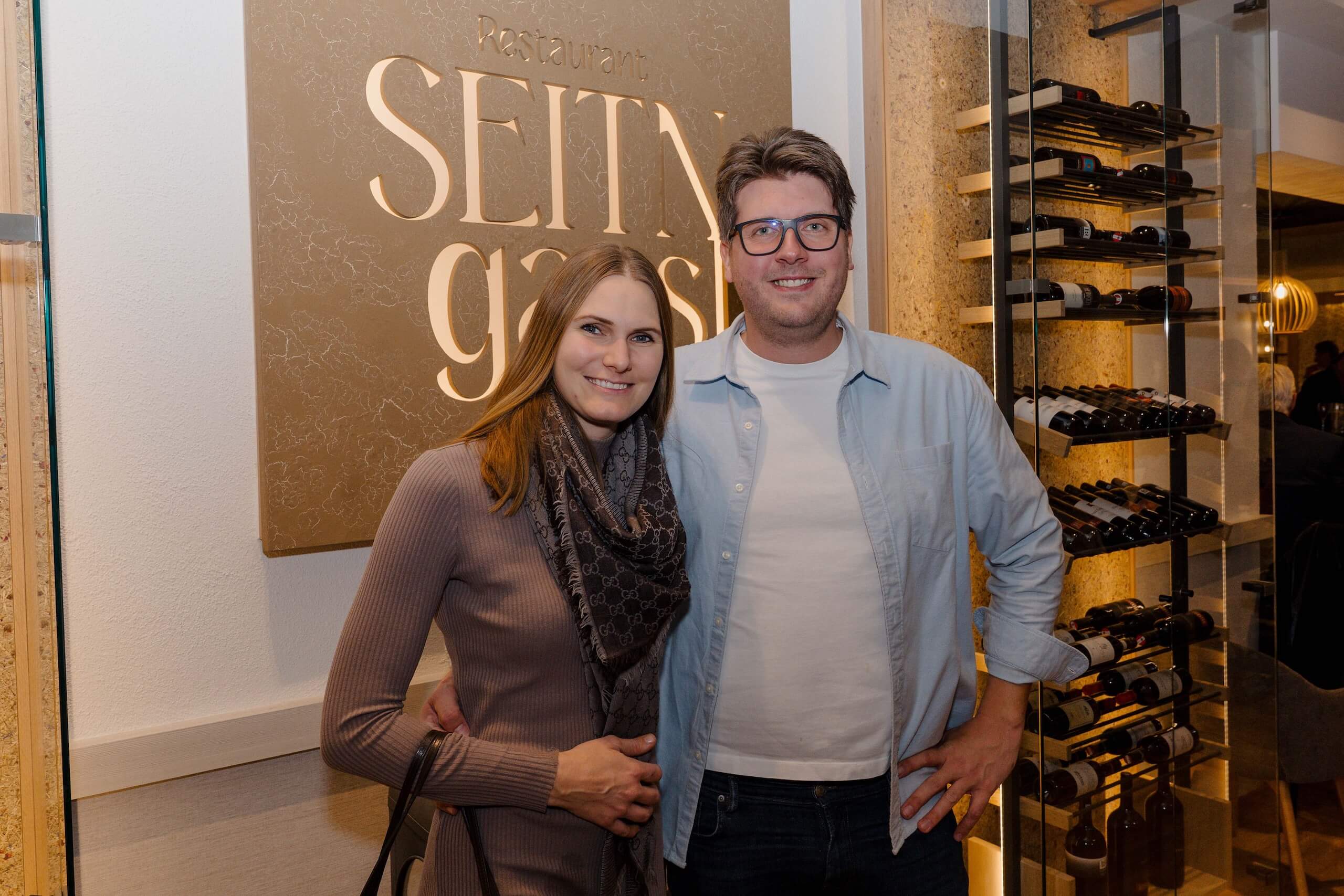 Paar vor Restaurant-Schild, idealer Ort für Hochzeitsfeiern mit stilvollem Ambiente und exklusiver Weinauswahl.