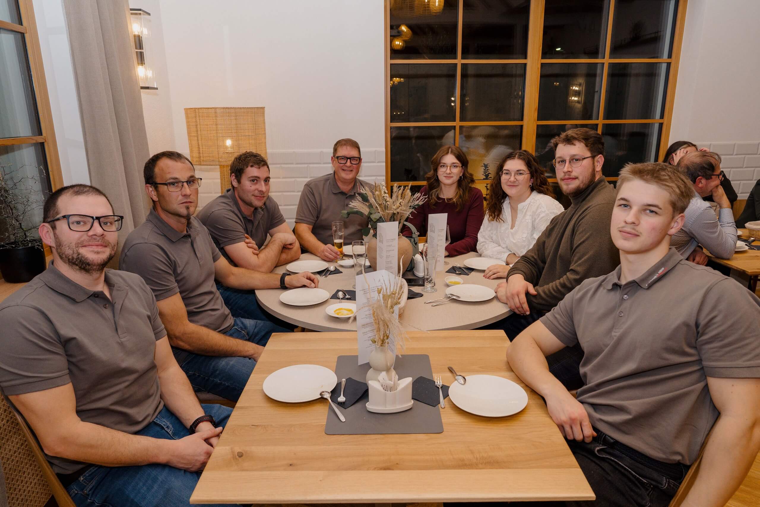 Gruppe von acht Personen an einem gedeckten Tisch in einer eleganten Hochzeitslocation, lächelnd beim Festessen.