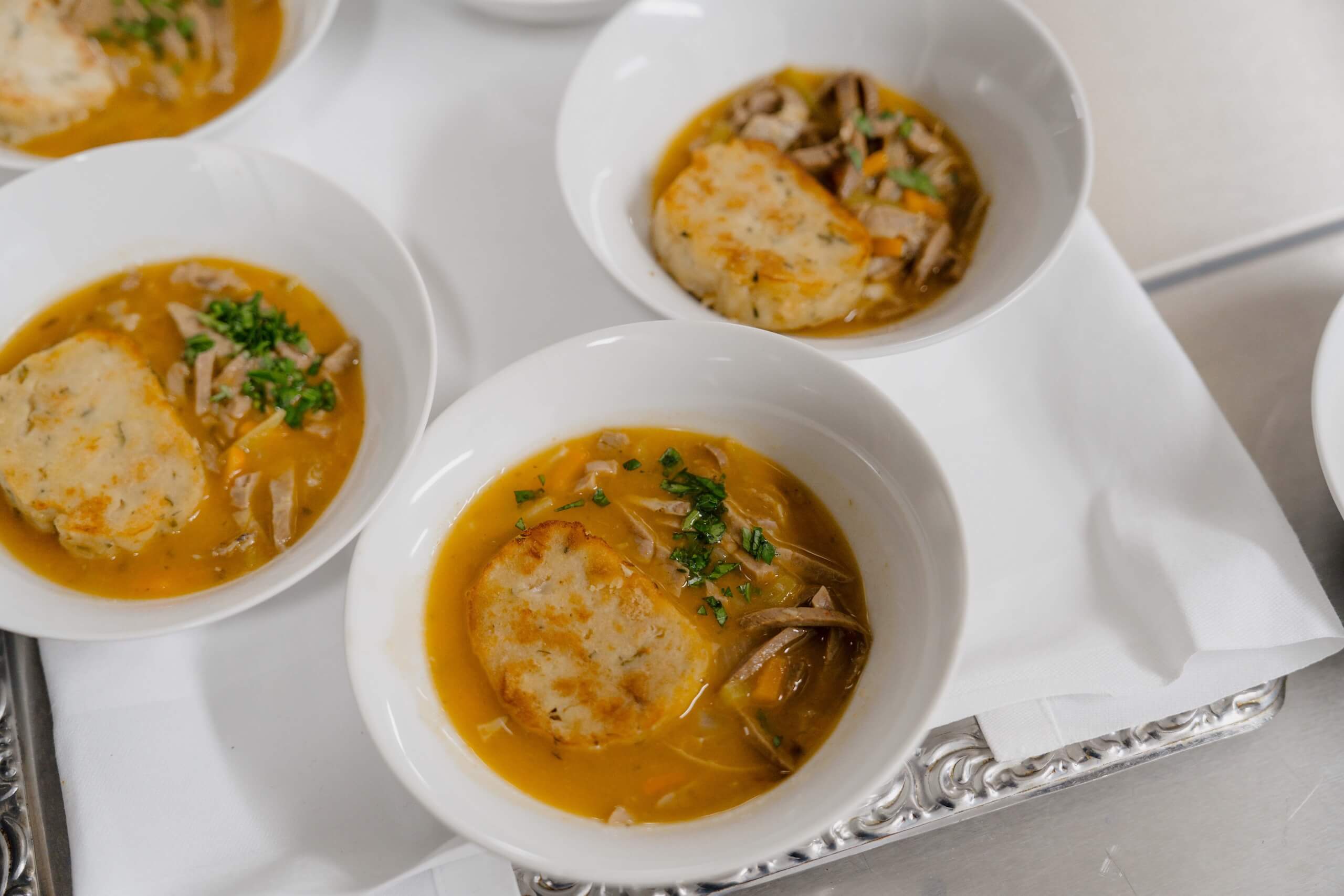 Elegante Hochzeitssuppe in weißen Schalen, dekoriert mit Kräutern, perfekt für eine stilvolle Hochzeitsfeier.