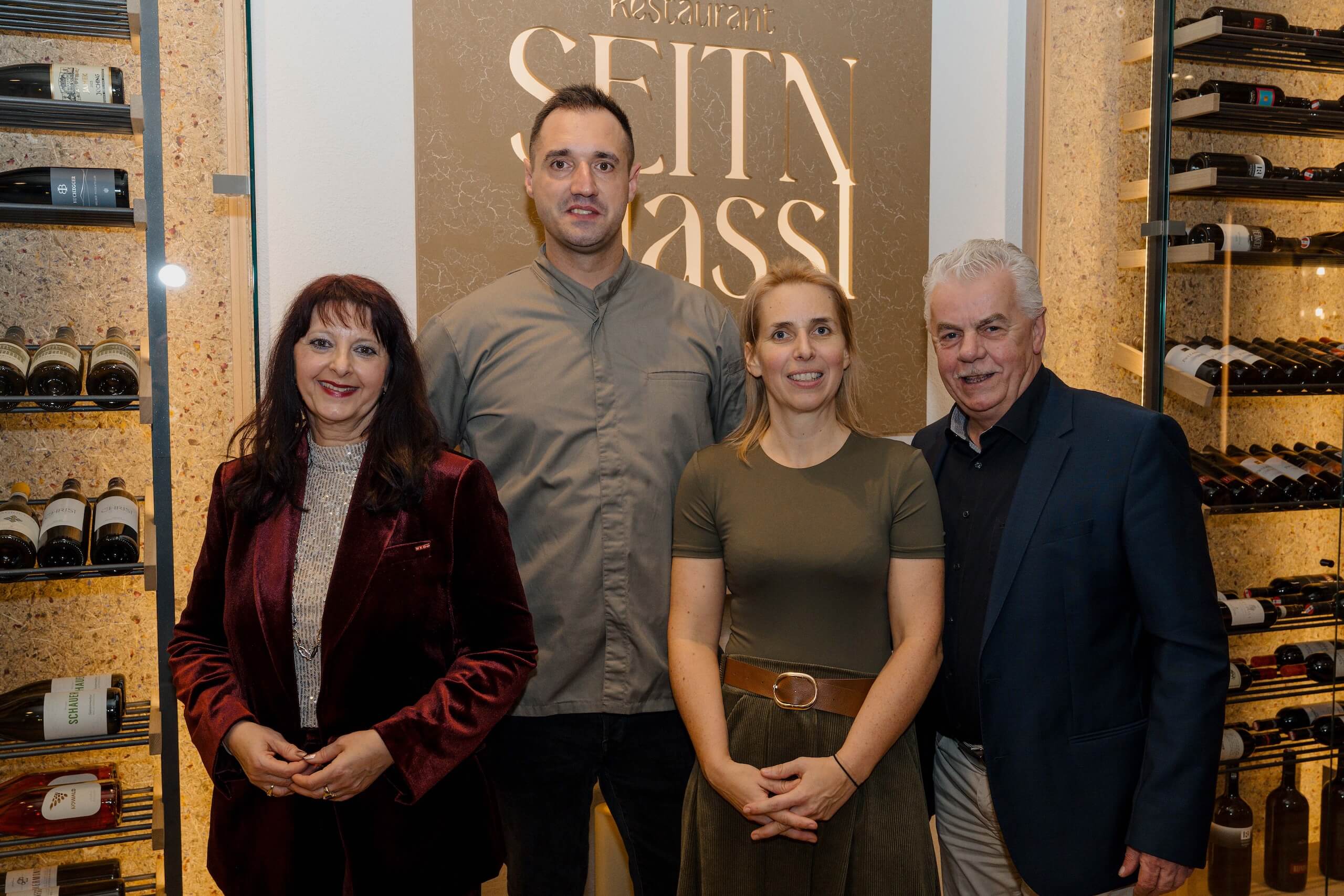 Gruppe lächelt vor Weinregal im Restaurant, perfekte Kulisse für eine stilvolle Hochzeit oder Feier bei Hochzeitstraum.
