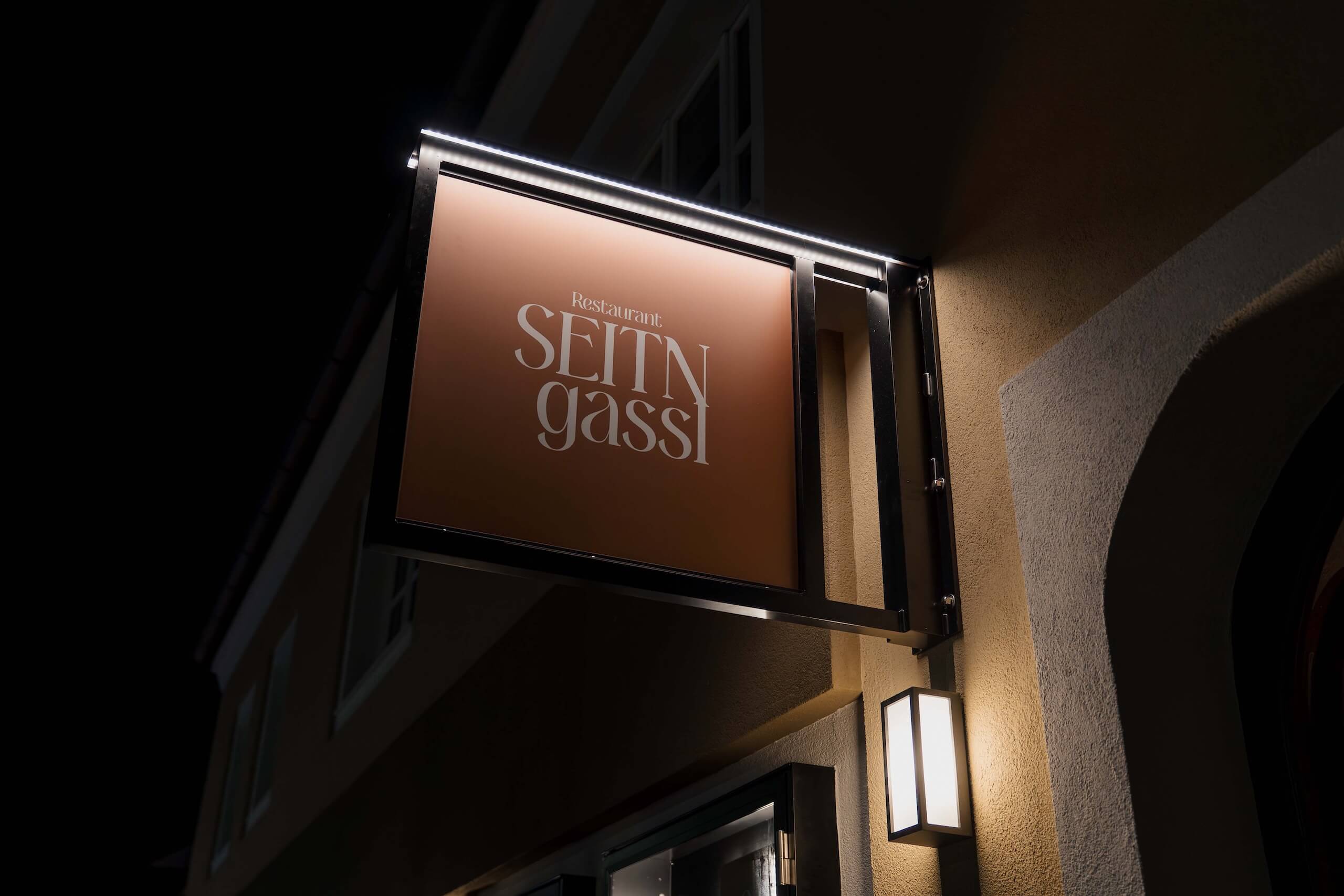 Beleuchtetes Schild des Restaurants Seintn Gassi, eine potenzielle Hochzeitslocation bei Nacht mit charmantem Ambiente.