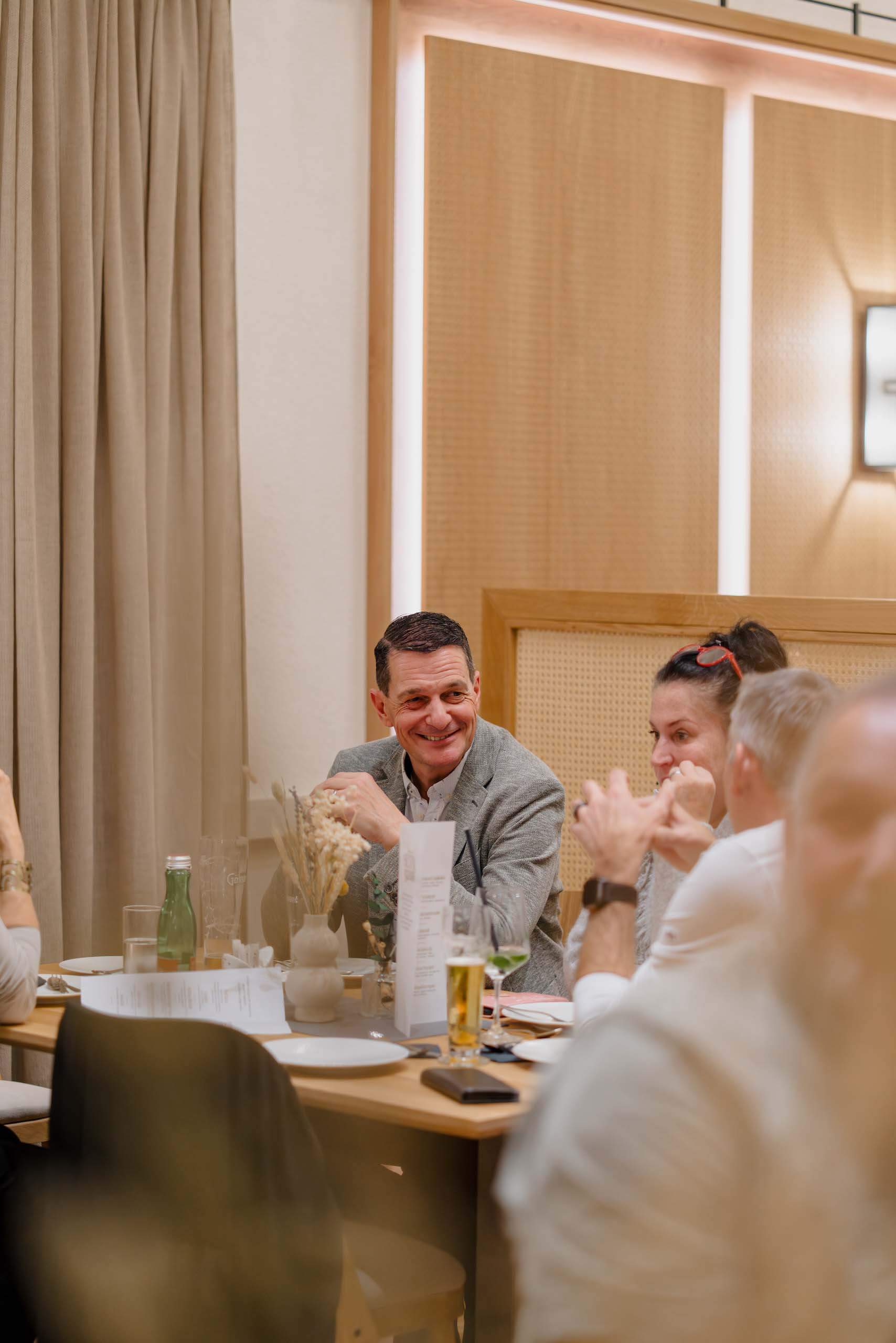 Gäste sitzen lächelnd an einem Tisch bei einer Hochzeitsfeier in einer stilvollen Location, Hochzeitsdekoration erkennbar.