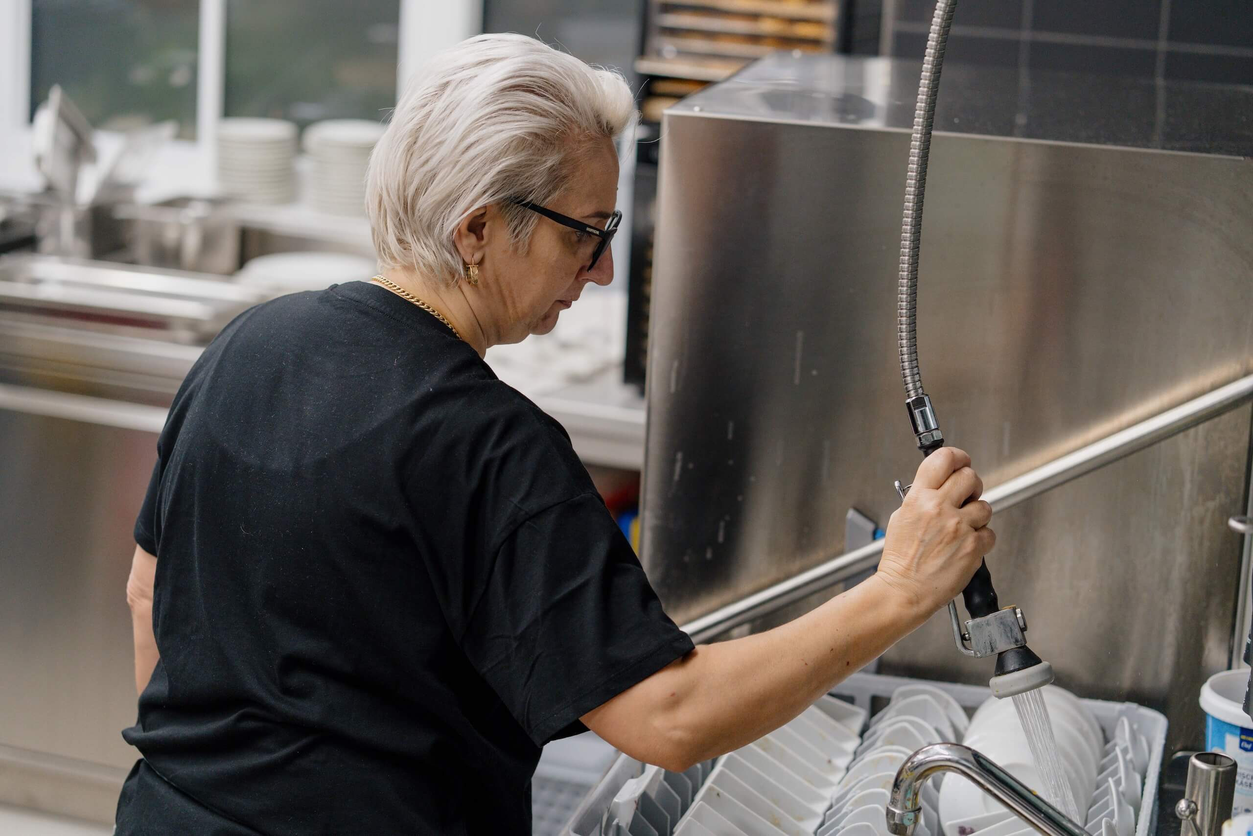 Angestellte spült Geschirr in Küche einer Hochzeitslocation für perfekt organisierte Feier bei Hochzeitstraum.