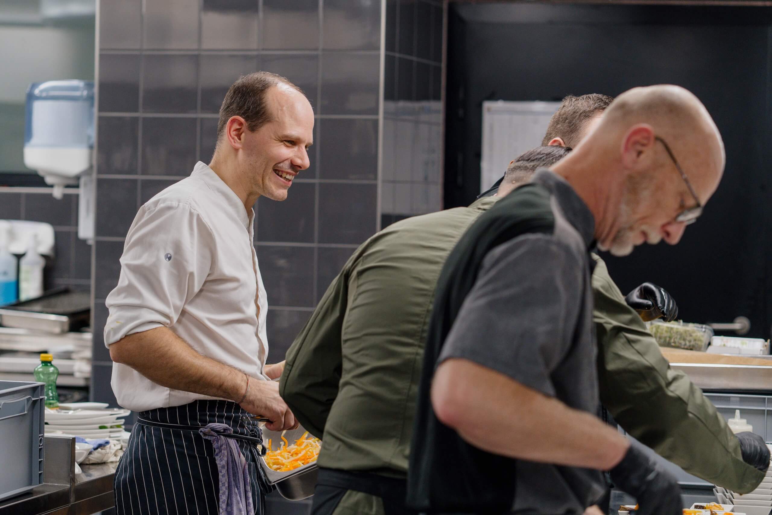 Köche bereiten in einer professionellen Küche mit Freude das Catering für eine Hochzeit vor. Perfekte Hochzeitslocation-Option.