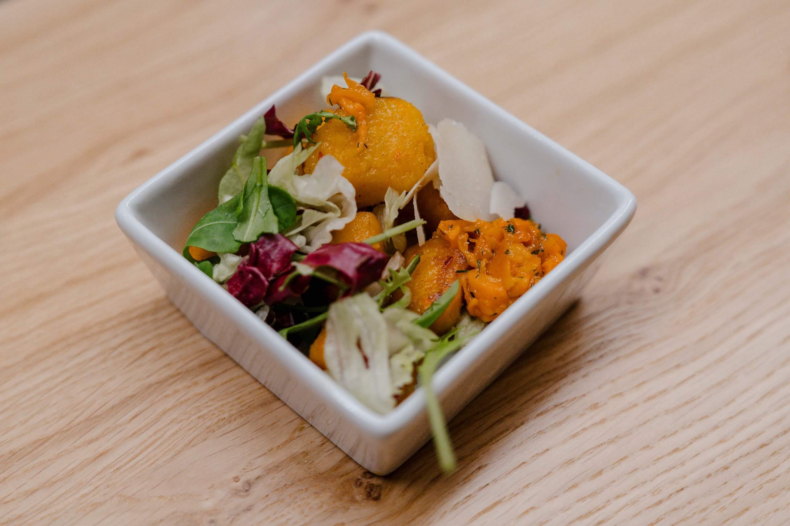 Frischer Salat mit zarten Kürbisgnocchi in weißer Schale, ideal für elegante Hochzeitsfeiern, präsentiert auf Holzuntergrund.